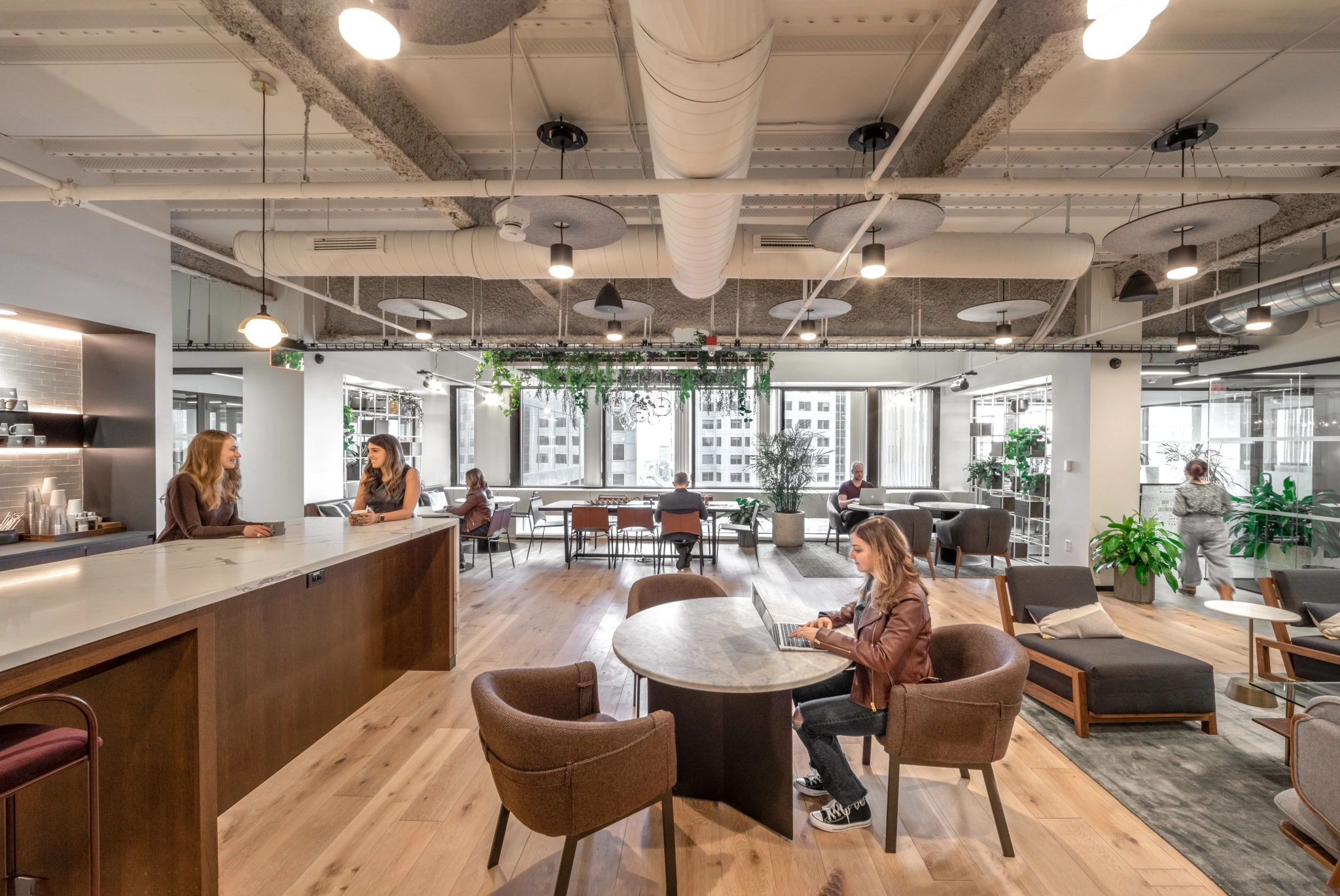 A spacious office space in Boston filled with individuals working collaboratively at tables.