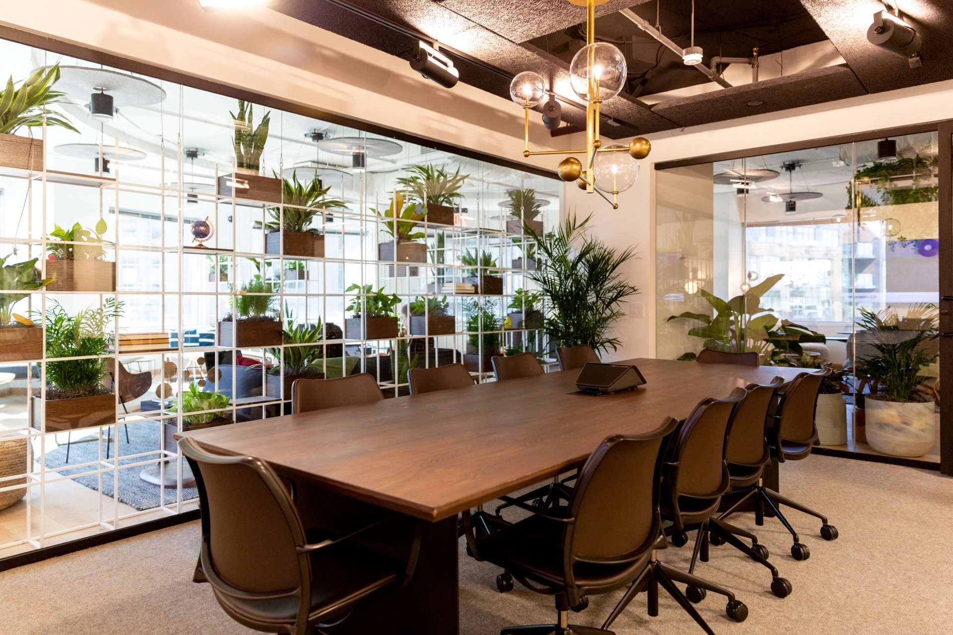 Une salle de réunion de coworking avec un mur de verre et des plantes luxuriantes.