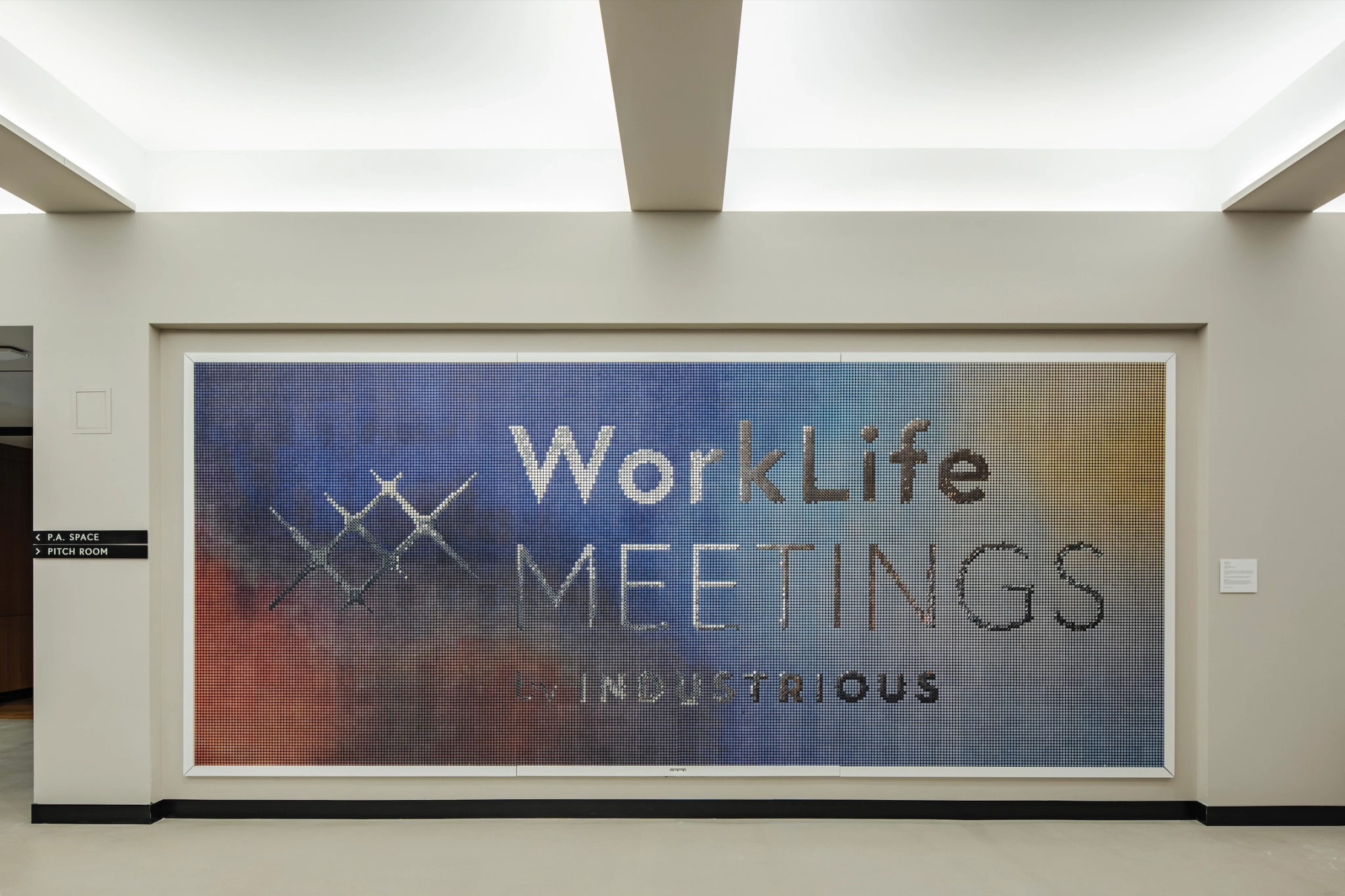 Une fresque murale dans les bureaux de New York affiche le texte « WorkLife Meetings by Industrious » avec des couleurs abstraites en arrière-plan, renforçant l'atmosphère vibrante de la salle de réunion.