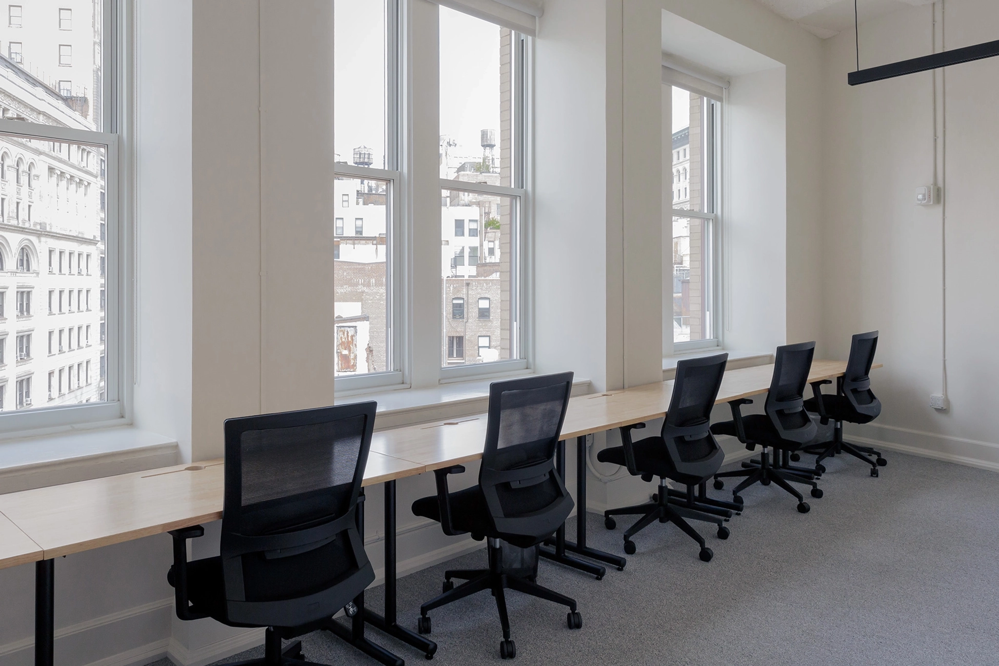 A spacious coworking workspace in New York adorned with sleek black desks and lined with large windows.