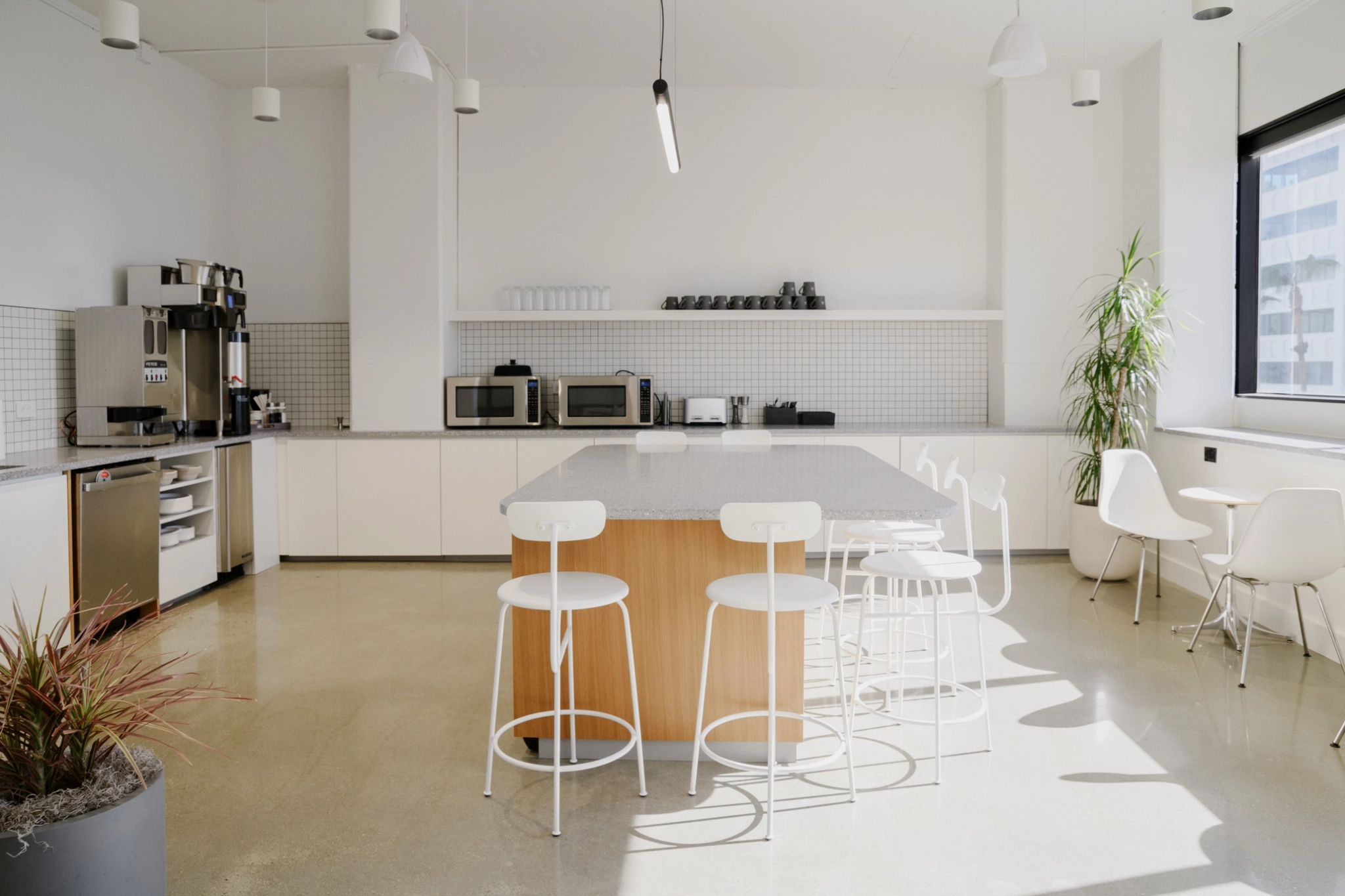 A white kitchen designed as a coworking workspace featuring stools and a table.