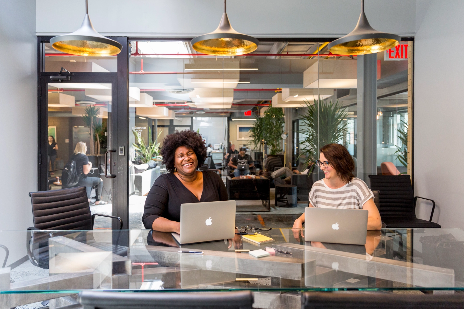 Two women working at an office table with laptops in a coworking space.