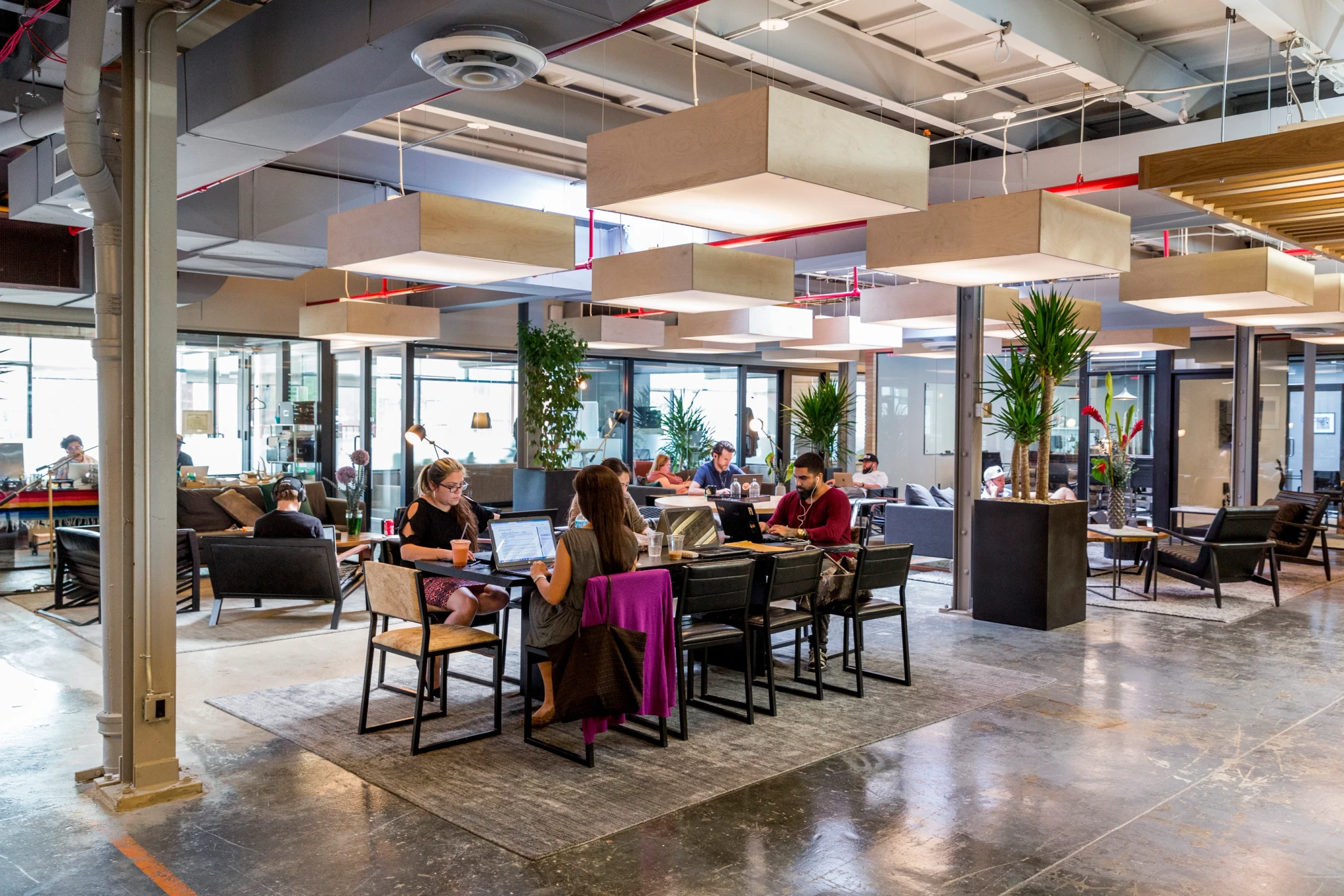 A spacious coworking area in Brooklyn with individuals working at communal tables.