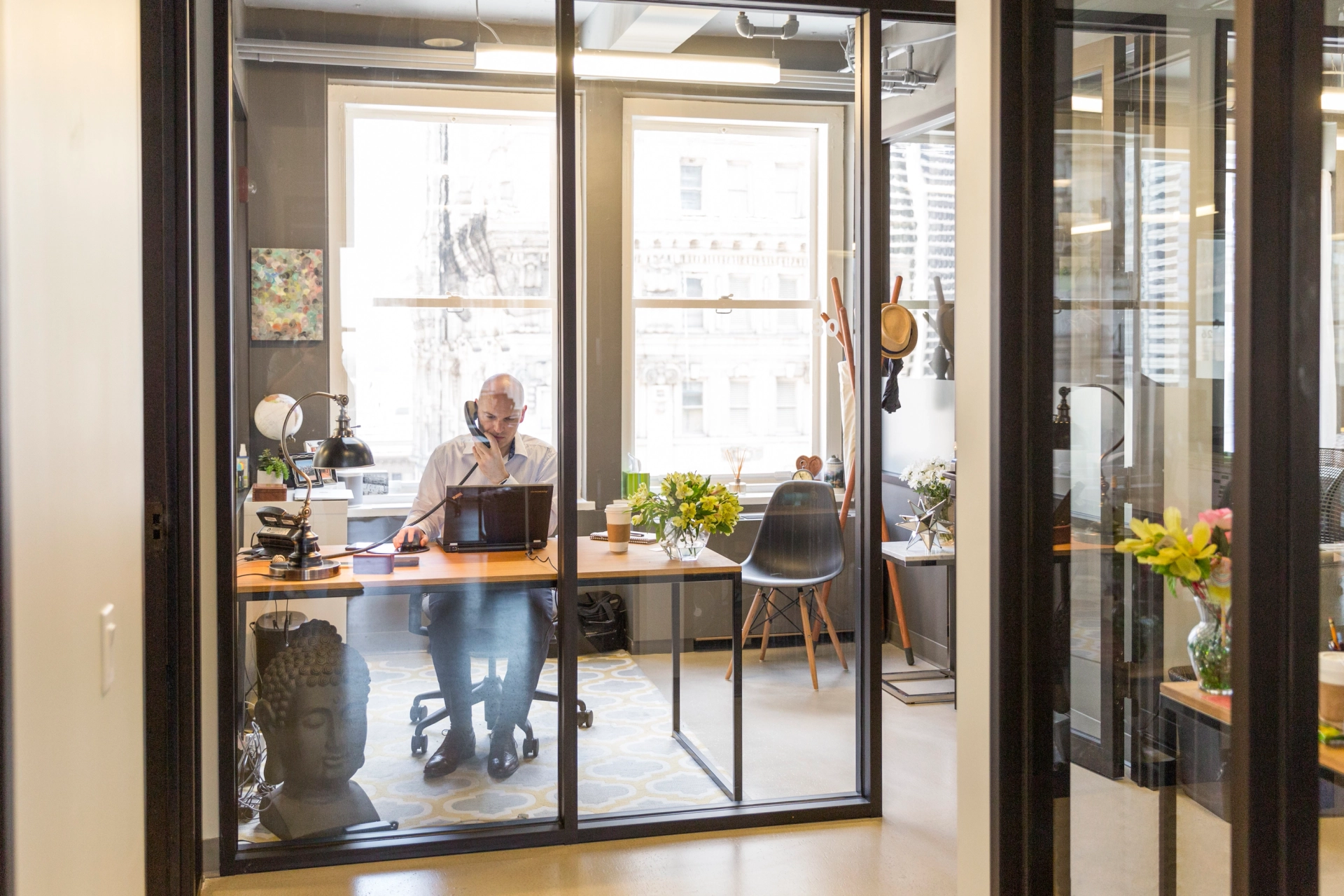 A man sits at a [office] desk in a [Philadelphia] office with glass doors.