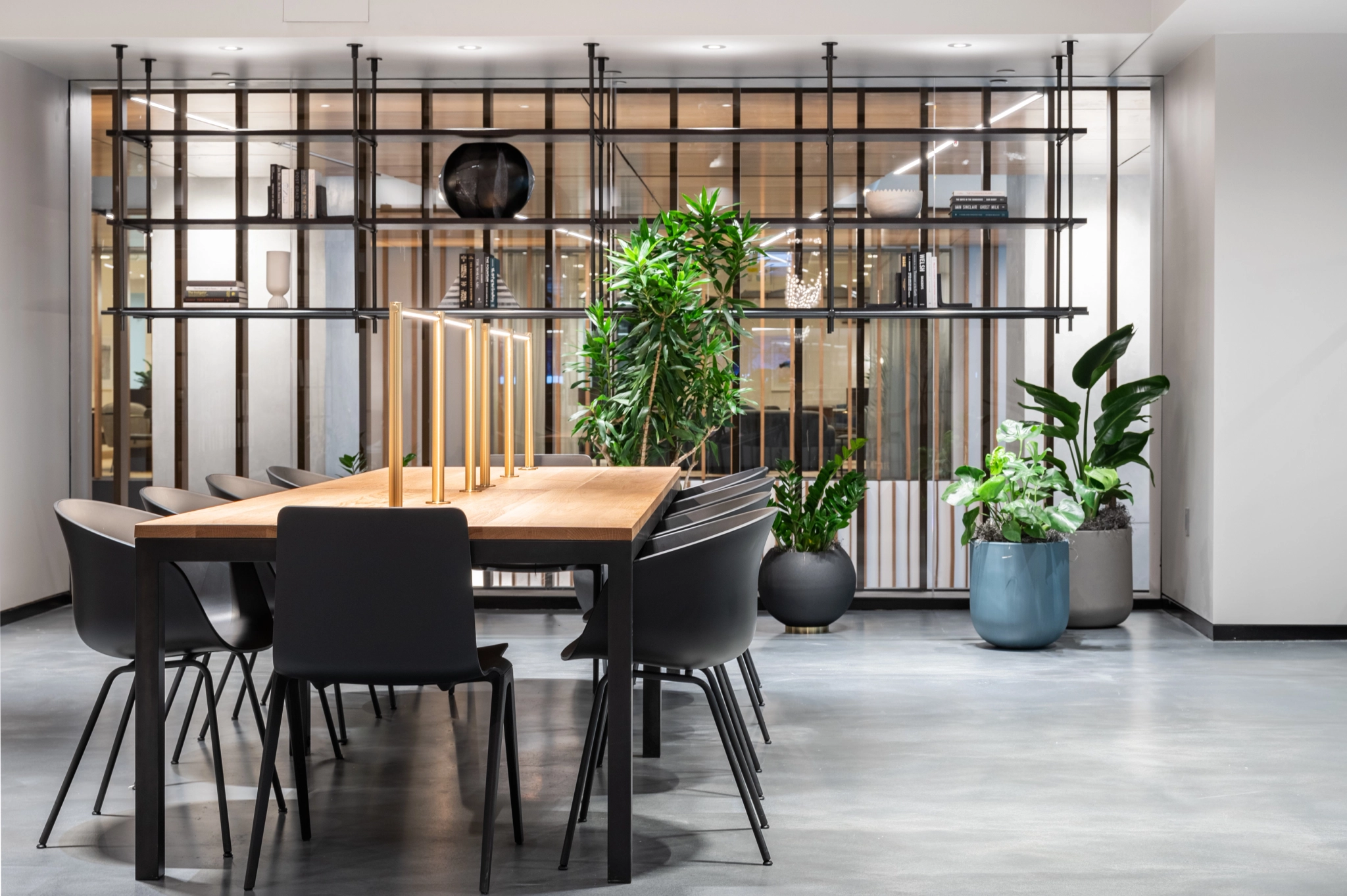 Salle de conférence moderne à New York avec une longue table en bois, des chaises noires, des étagères décoratives et diverses plantes vertes. Un espace de travail parfait pour votre prochaine réunion.