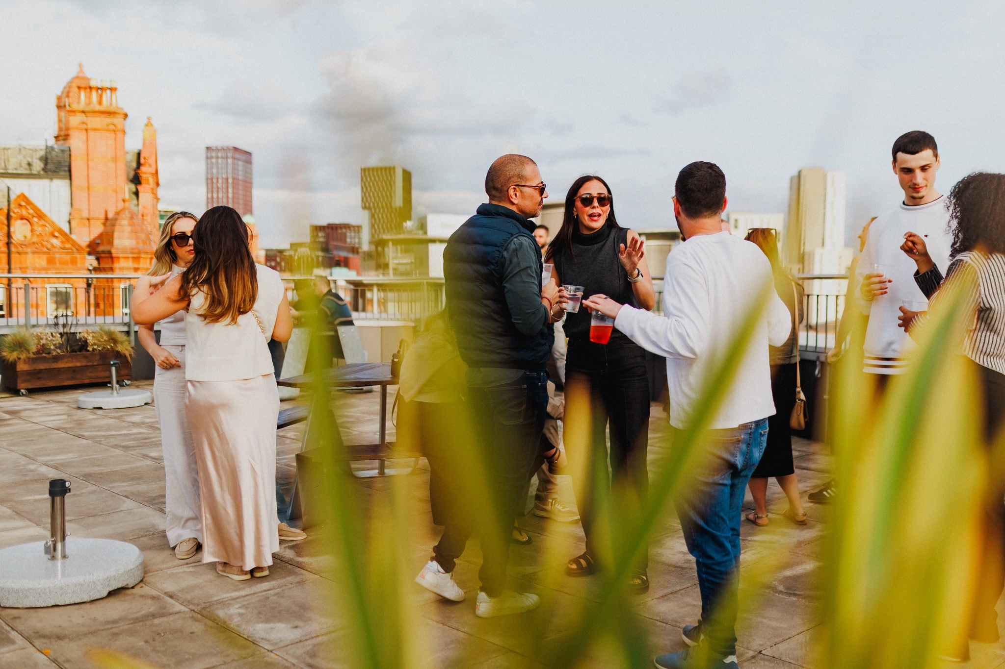 Un grupo de personas socializa en una azotea de la ciudad durante el día, algunas con una copa en la mano, con edificios y vegetación de fondo: un espacio de coworking dinámico que combina relajación y productividad.