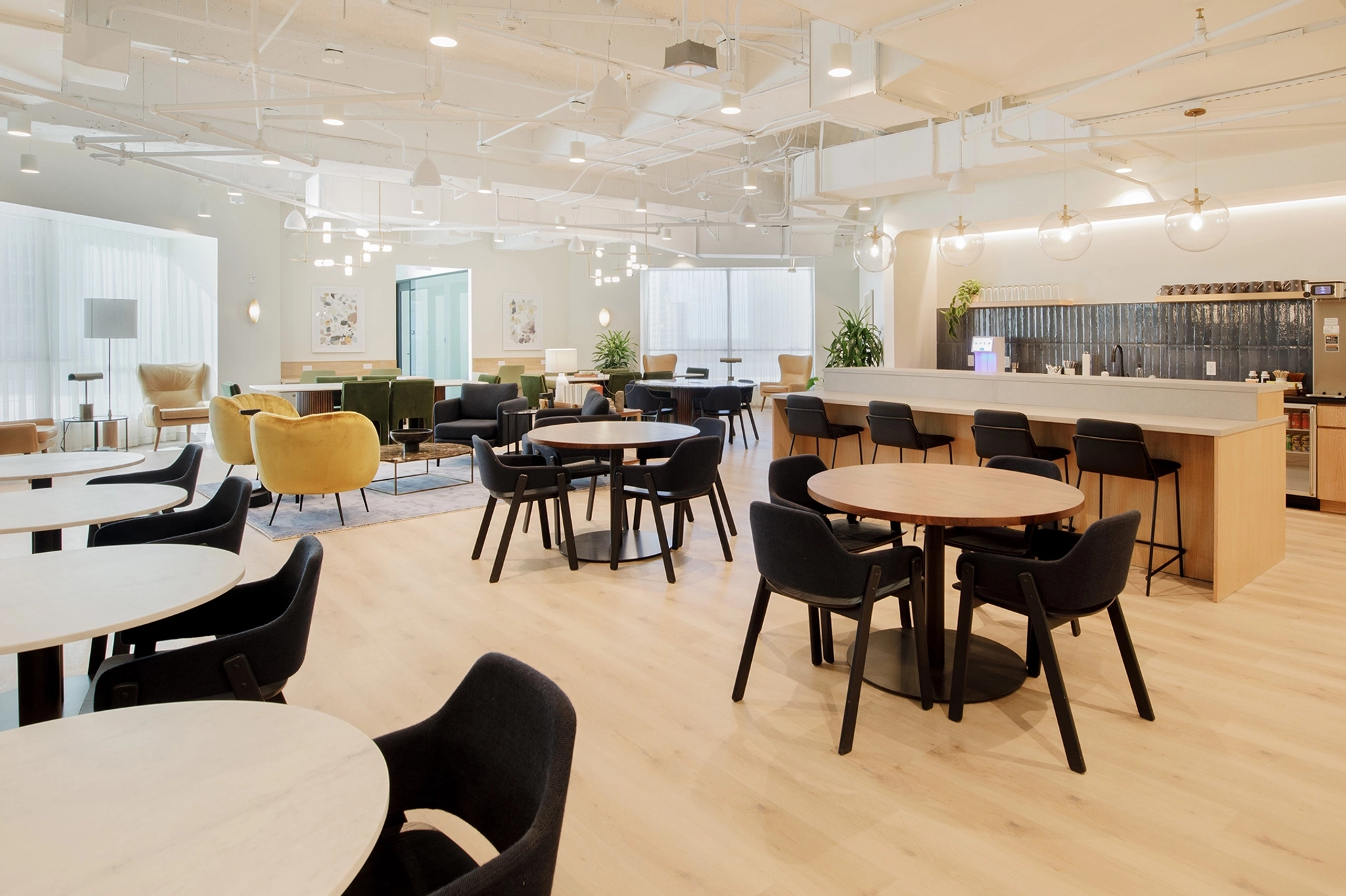 A modern coworking lounge in Fort Lauderdale featuring round tables, various seating options, a coffee bar, and natural lighting.