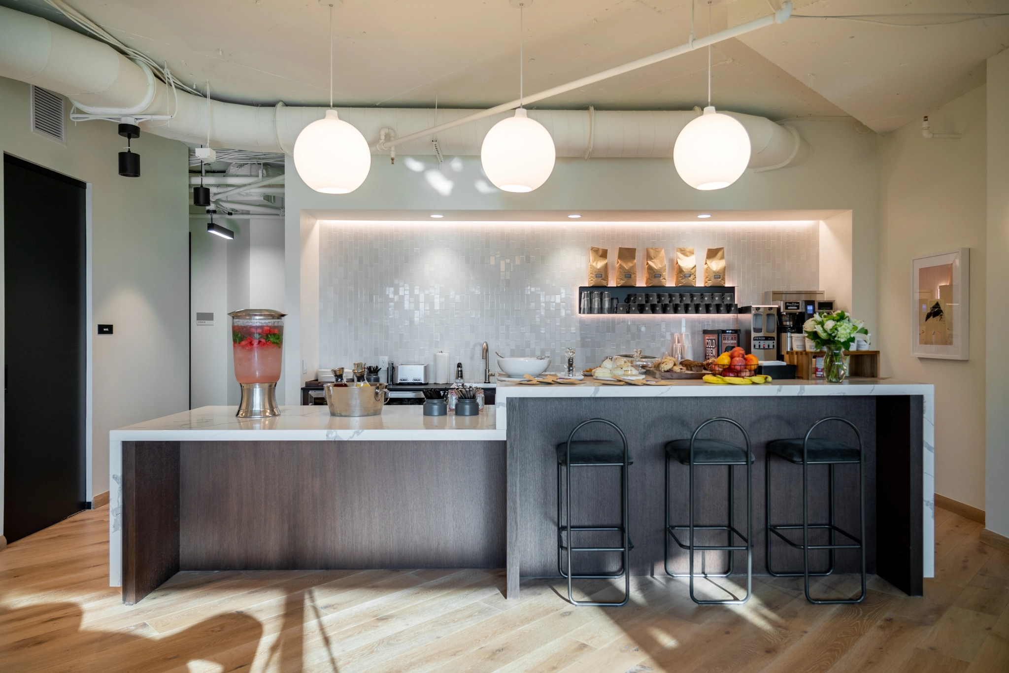 Moderne kantoorkeuken in McLean met een groot kookeiland, drie hoge stoelen, hanglampen, een drankautomaat en diverse snacks en fruitsoorten: perfect voor coworkingpauzes.