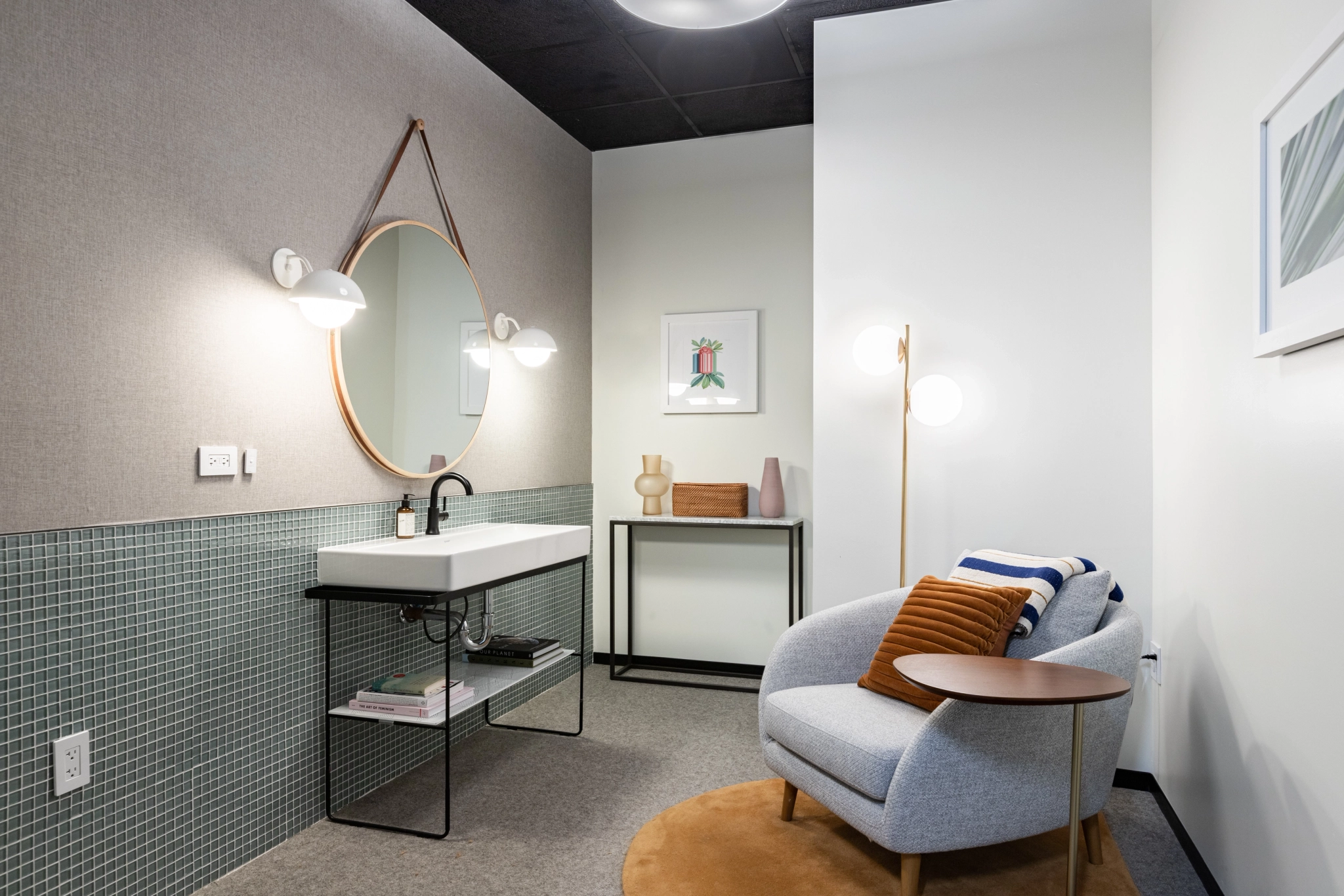 Moderne badkamer met ronde spiegel en zithoek, ontworpen voor coworking-ruimtes.