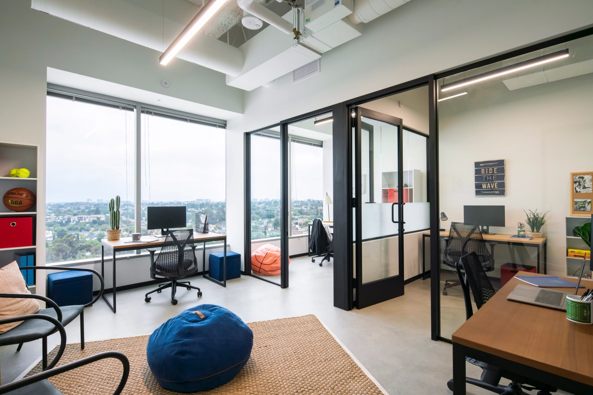 Moderne coworkingruimte in Los Angeles met glazen scheidingswanden, individuele werkplekken en uitzicht op het stadsbeeld door grote ramen. Ook is een informele zithoek met zitzakken zichtbaar.