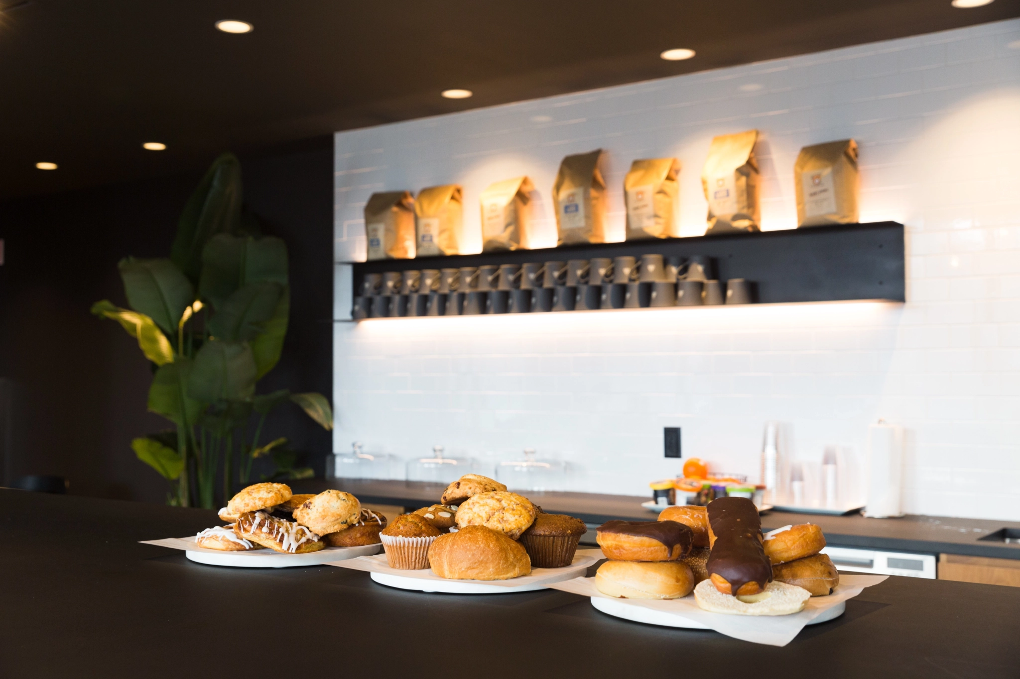 Eine Theke im Konferenzraum des Büros ist mit verschiedenen Backwaren, darunter Muffins, Eclairs und Donuts, dekoriert. Kaffeetüten und gestapelte Tassen stehen auf Regalen vor einer weiß gekachelten Wand im Hintergrund und fangen die geschäftige Atmosphäre eines Chicagoer Morgens ein.