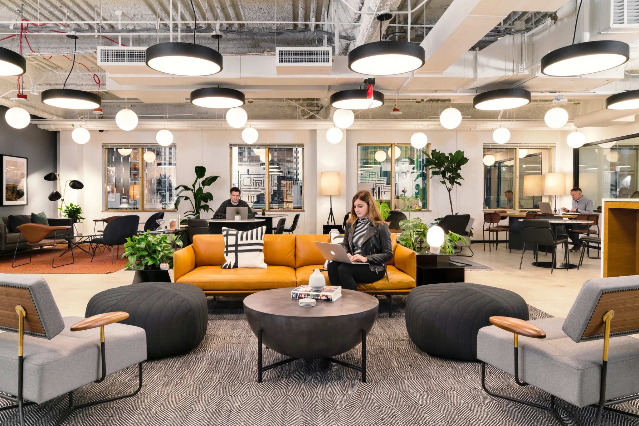 Een moderne werkplek in Seattle met mensen die op laptops werken. Bijzonderheden zijn onder meer ronde lampen, grijze stoelen, een mosterdkleurige bank en planten.