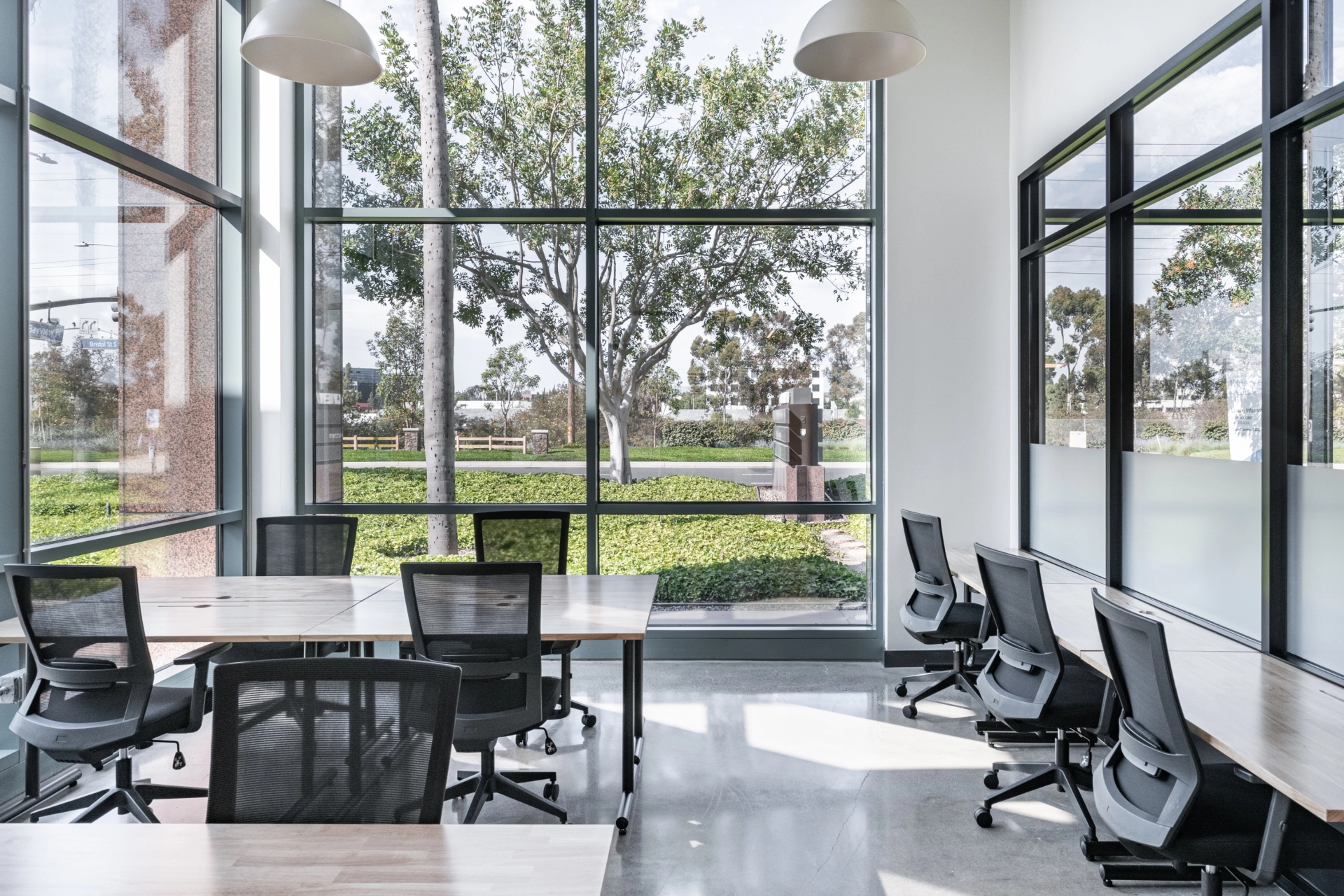Une salle de réunion de coworking à Newport Beach avec de grandes fenêtres et des chaises noires.