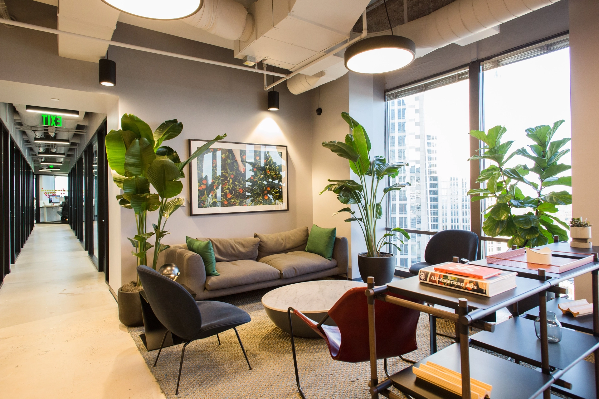Moderne coworking-lounge met comfortabele stoelen en potplanten bij een raam met uitzicht op de stad.