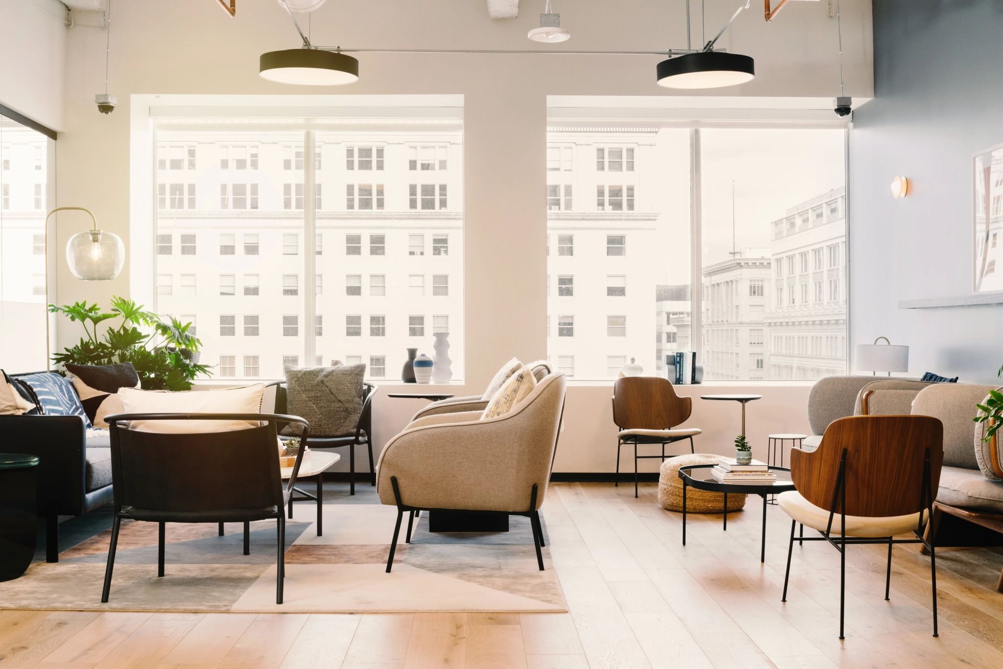 Eine moderne, gut beleuchtete Bürolounge in Portland mit großen Fenstern, modernen Möbeln und Zimmerpflanzen. Die Sitzgelegenheiten bestehen aus Stühlen und Sofas, die um kleine Tische angeordnet sind und sich ideal für einen entspannten Arbeitsbereich oder einen informellen Besprechungsraum eignen.