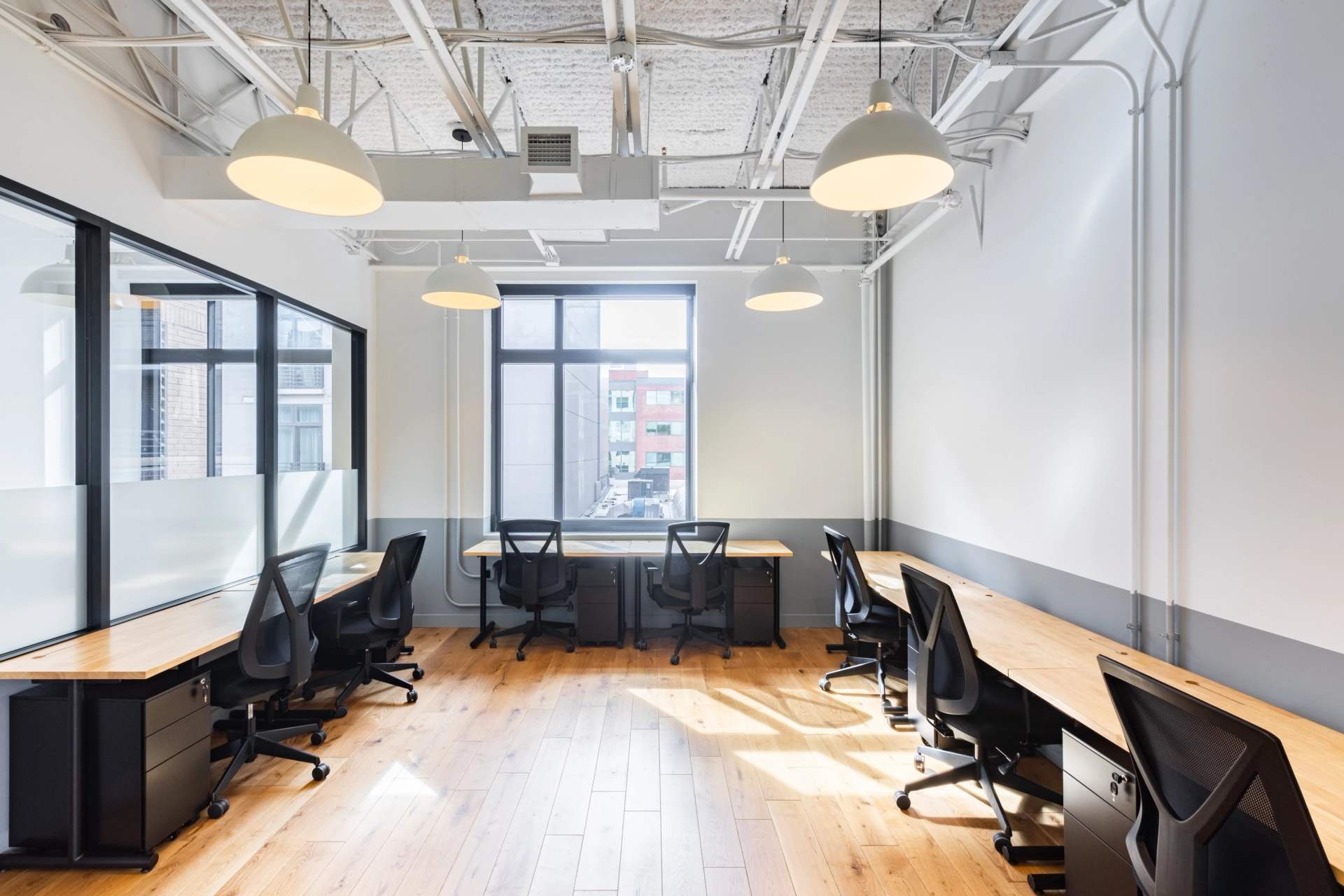 An open office with workspaces featuring wooden floors and black desks.