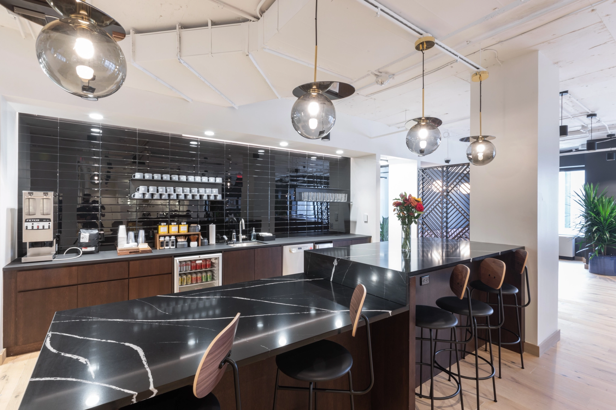 A black and white kitchen in an office setting with stools and a bar.