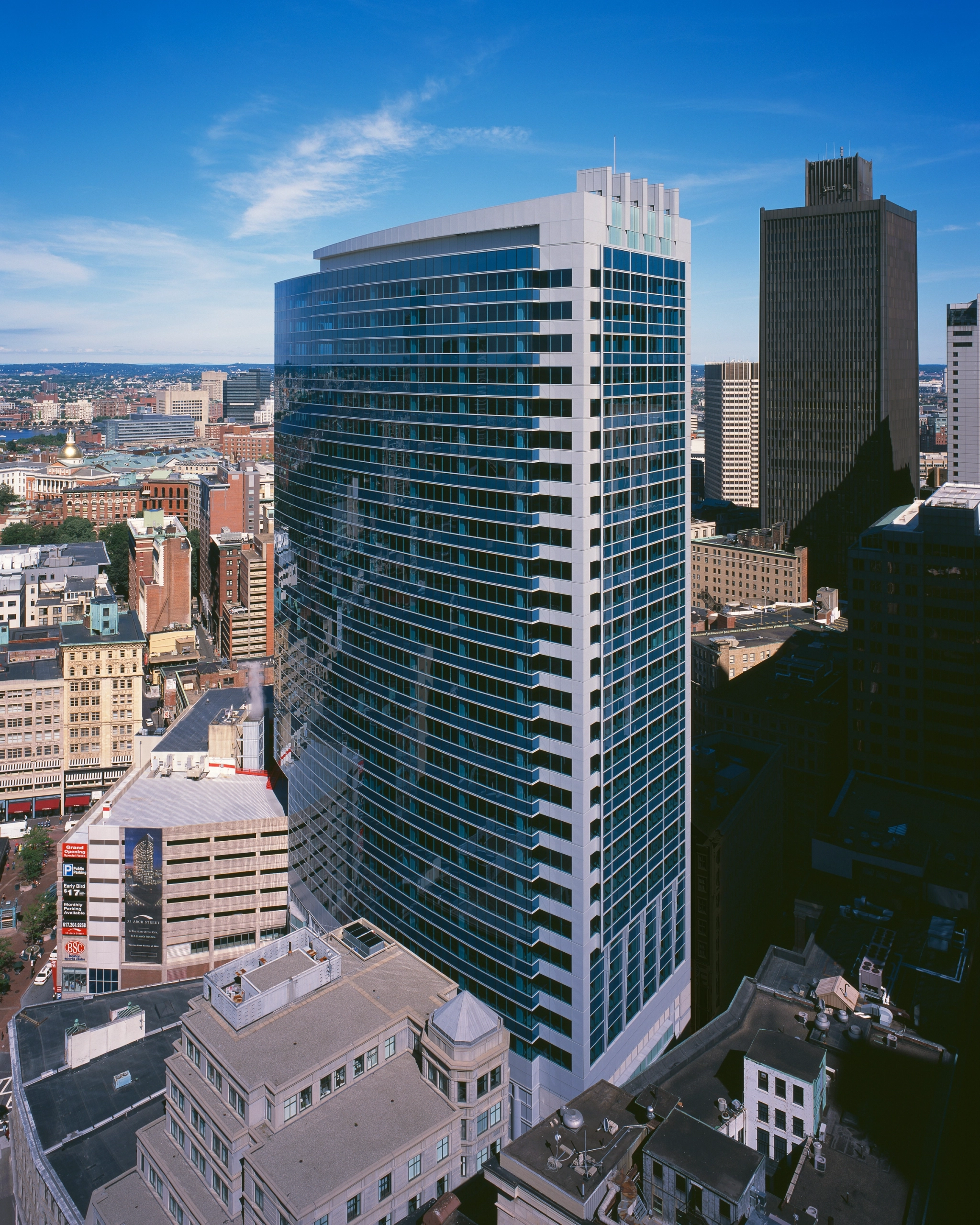 Tall modern skyscraper with glass facade, housing sleek office spaces and coworking areas, amidst other buildings in an urban cityscape on a clear day.