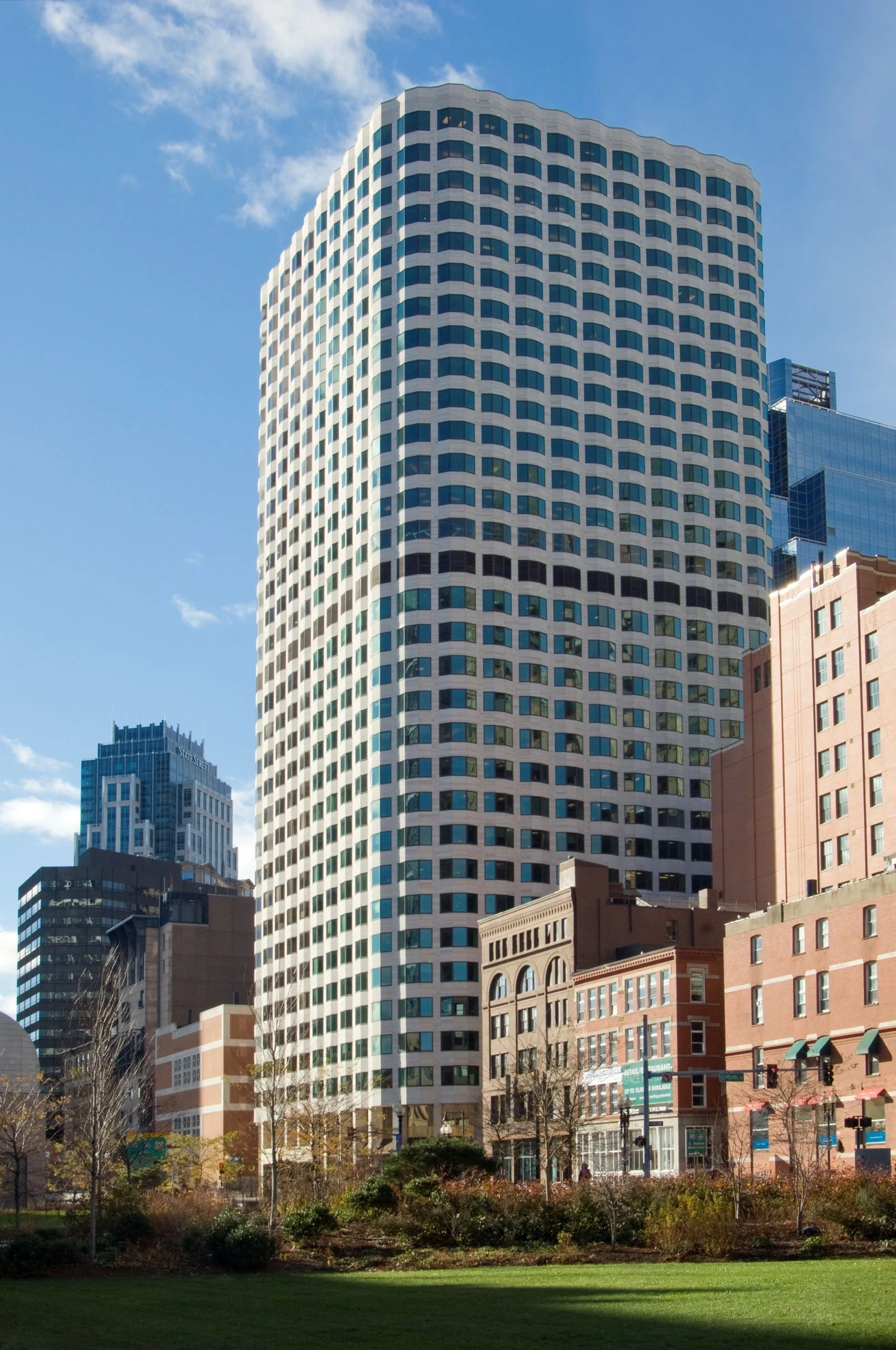 A tall, modern glass and steel office building stands amid other shorter buildings in an urban area of Boston, with a partly cloudy sky background. Inside, state-of-the-art meeting rooms cater to the high-paced corporate environment.