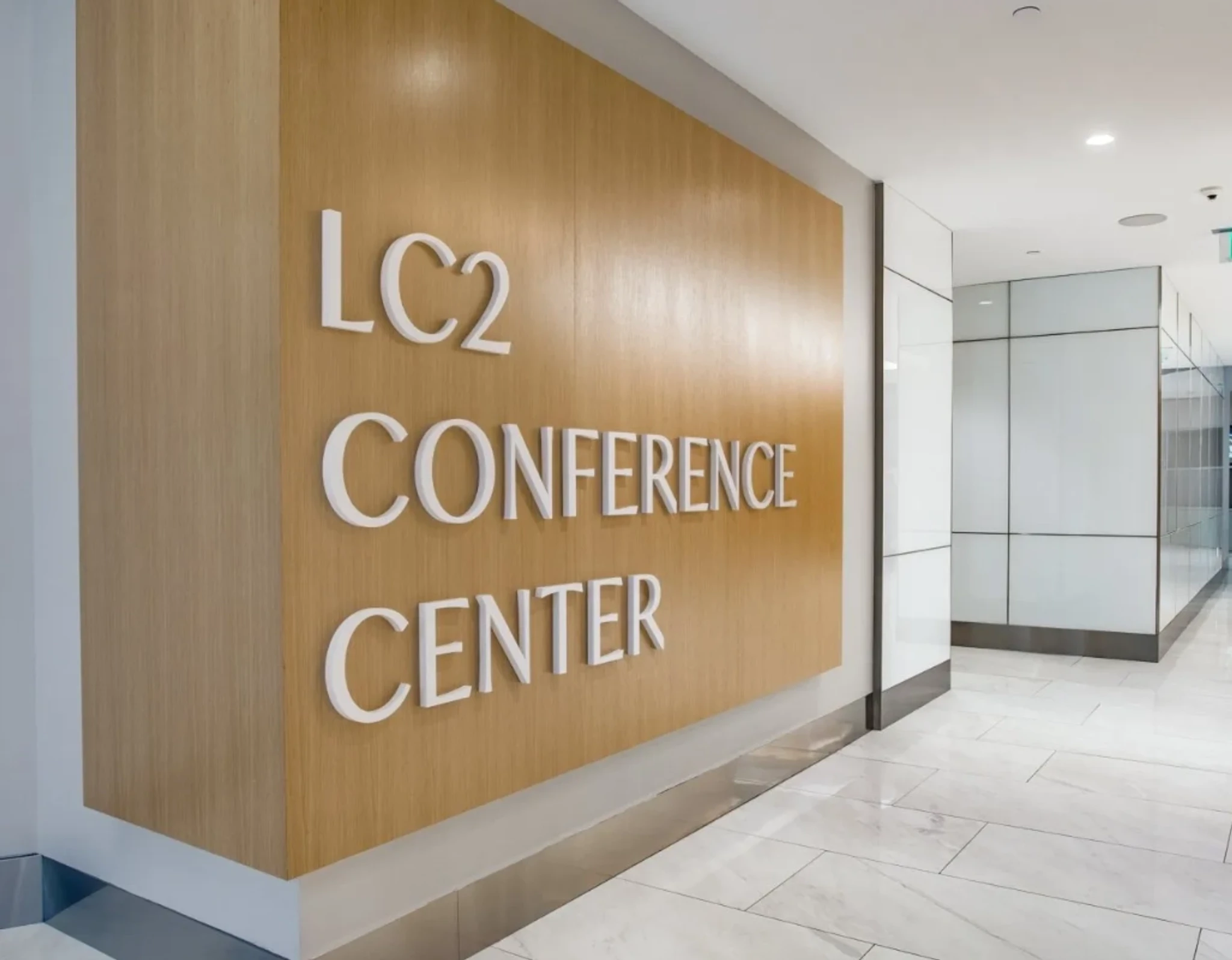 A wall sign reads "LC2 Conference Center" in a modern office hallway with white floors and glass-paneled walls.