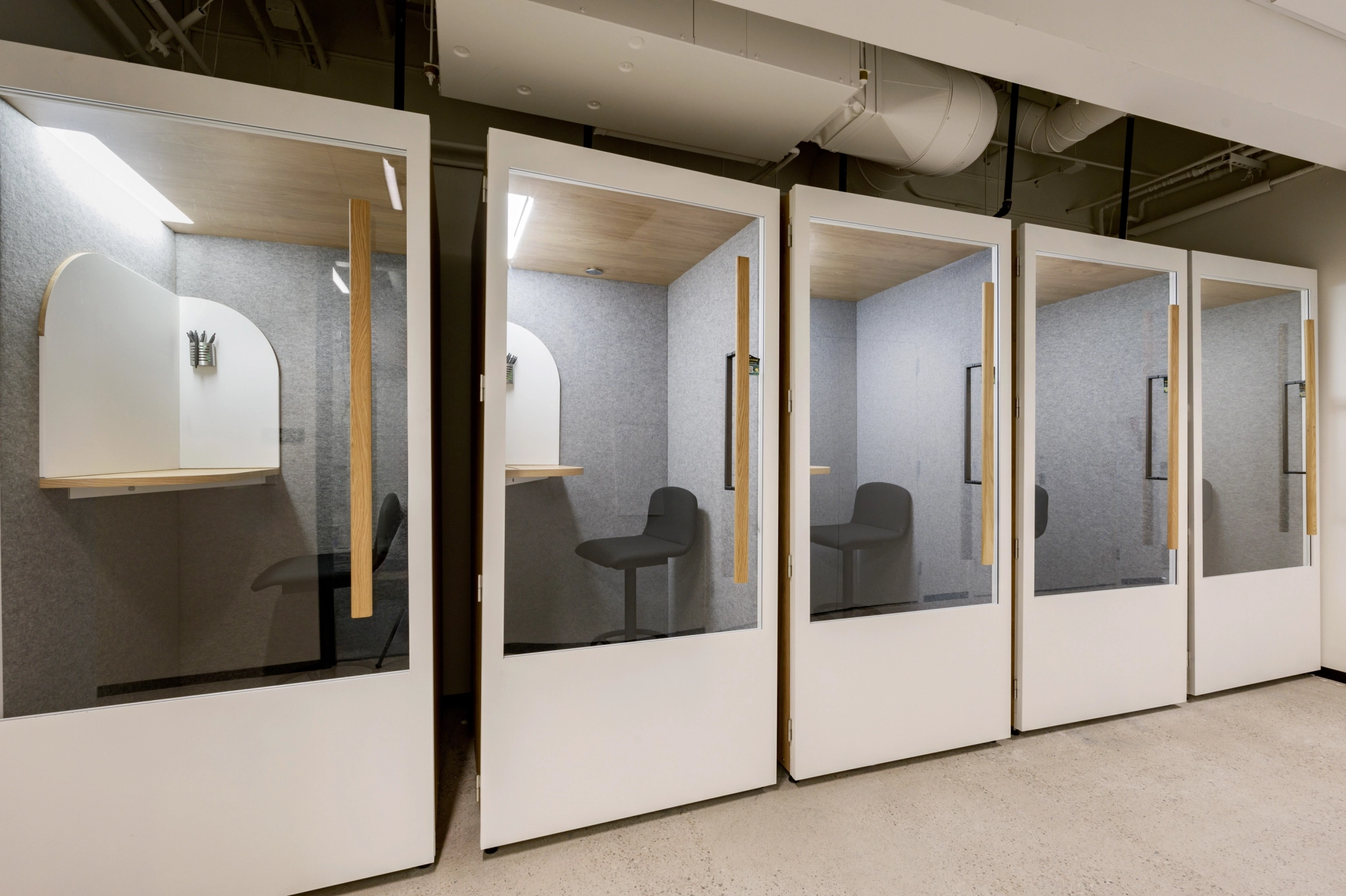 A row of modern, soundproof office pods with glass doors, wooden work surfaces, and stools in a clean and organized Chandler workspace environment.