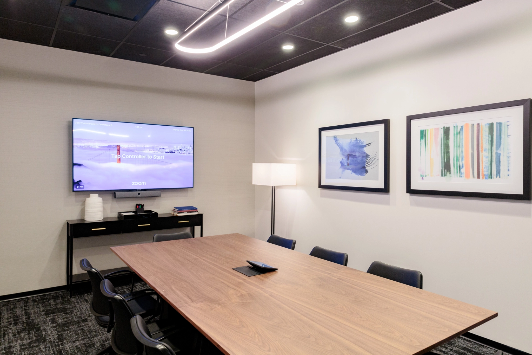 Moderne coworkingruimte in Brooklyn met een stijlvolle vergaderruimte met een houten tafel, zwarte stoelen, aan de muur gemonteerd scherm, abstracte kunst en staande lamp.