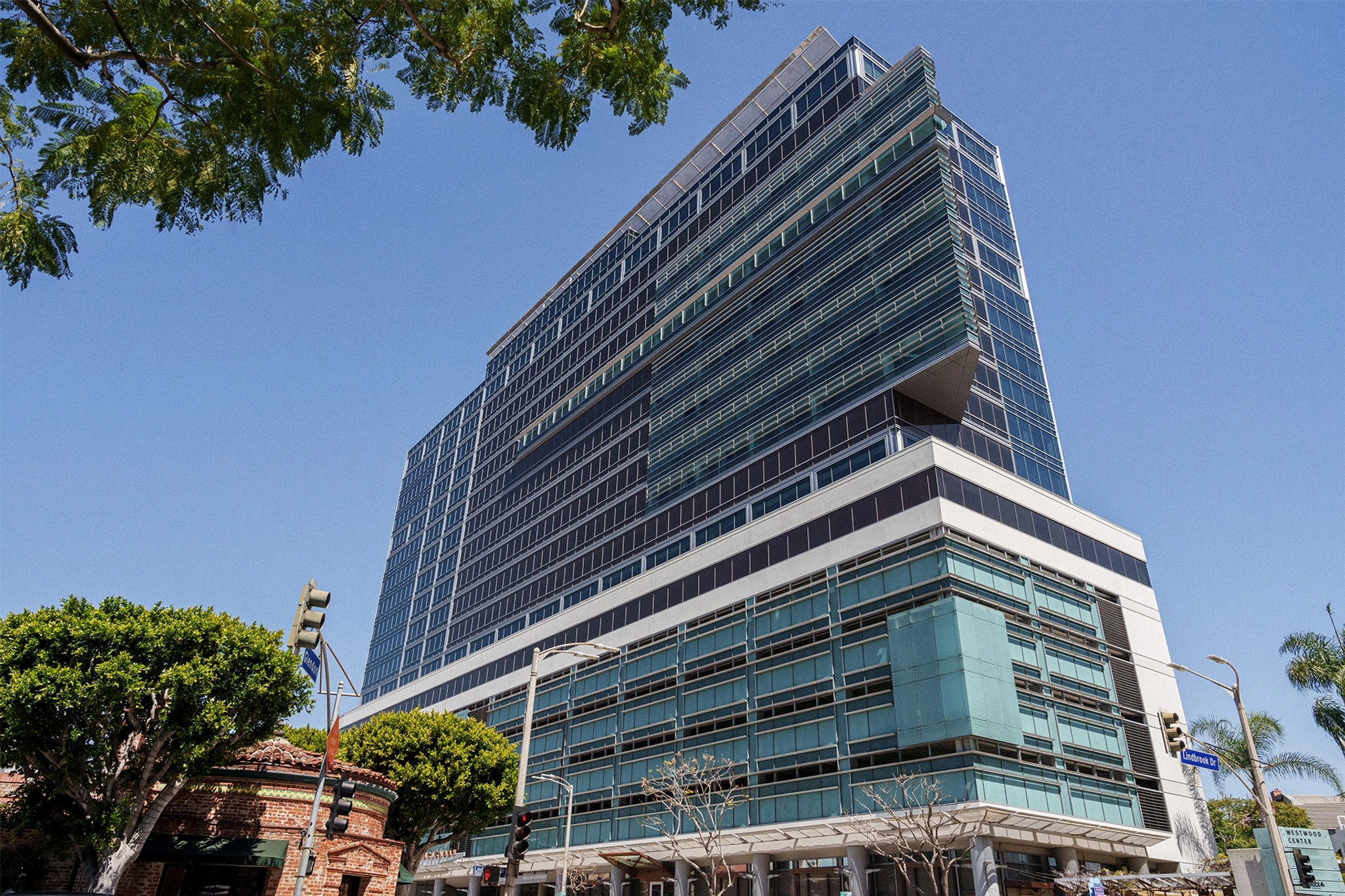 A modern multi-story office building with glass facades glistens under the clear Los Angeles sky, surrounded by trees and streetlights. Inside, sleek meeting rooms and dynamic workspaces cater to innovative professionals.