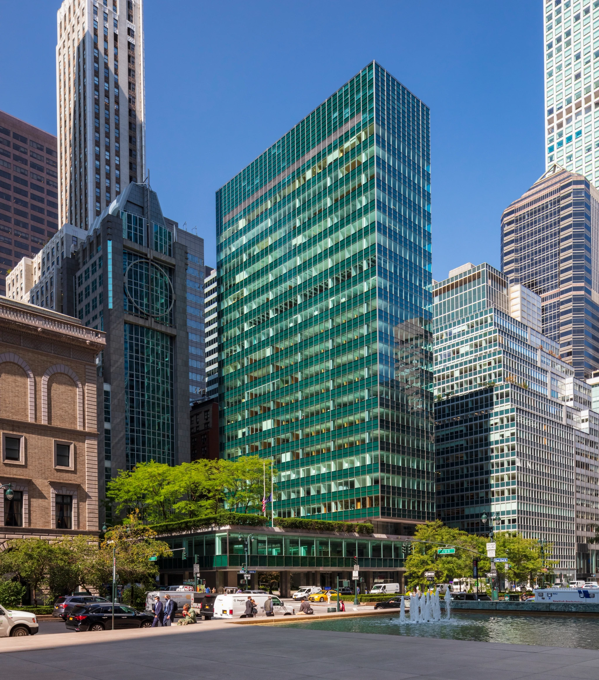 A modern glass office building with a green facade stands among other skyscrapers and historic buildings in New York, offering a vibrant workspace under a clear blue sky.