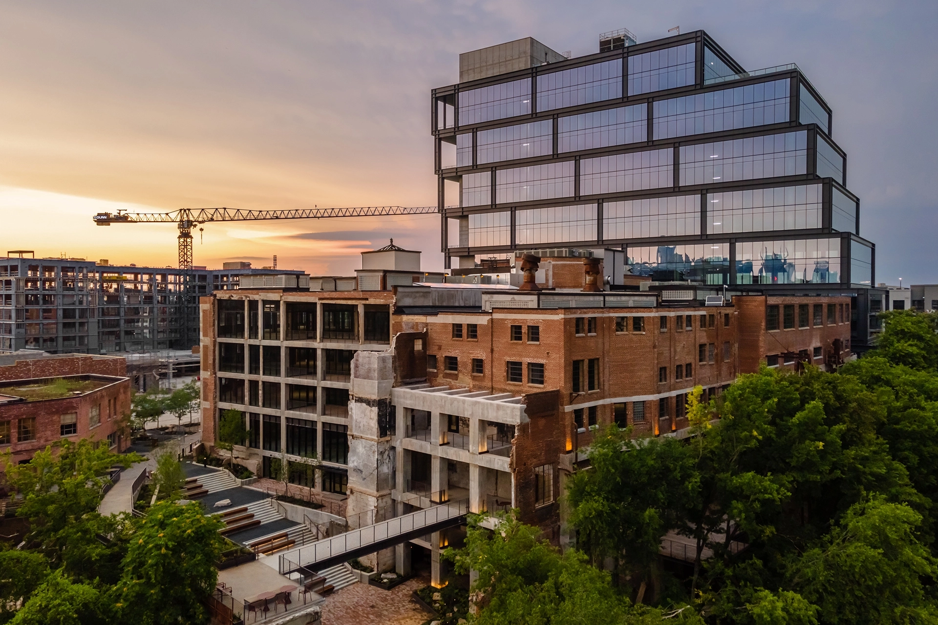 Un coucher de soleil urbain à Nashville mettant en valeur un mélange de vieux bâtiments en brique et une structure de bureaux moderne en verre, avec une construction en arrière-plan.