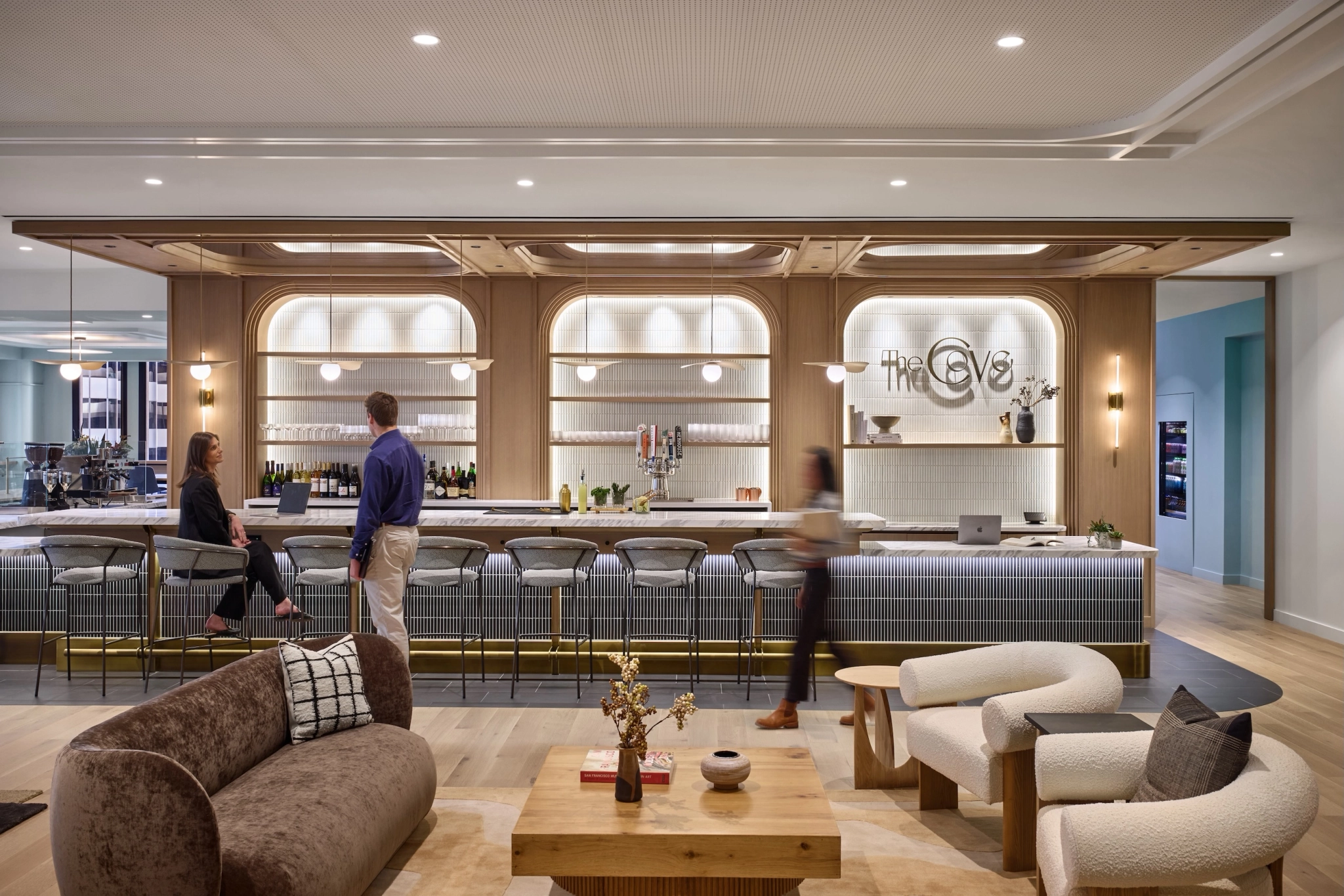 People are seated and standing in a modern San Francisco cafe with a long marble counter and shelves displaying bottles behind it, offering a perfect workspace for coworking.