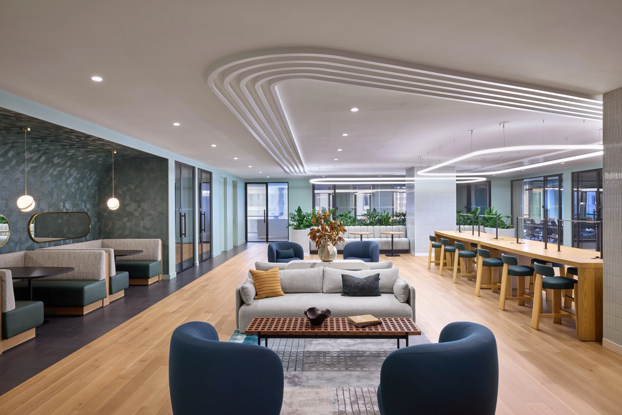 A modern lounge area in San Francisco with people sitting and standing, featuring tables, chairs, and a bar counter. This versatile workspace boasts a neutral color palette with green accents, perfect for casual meetings or collaborative work sessions.