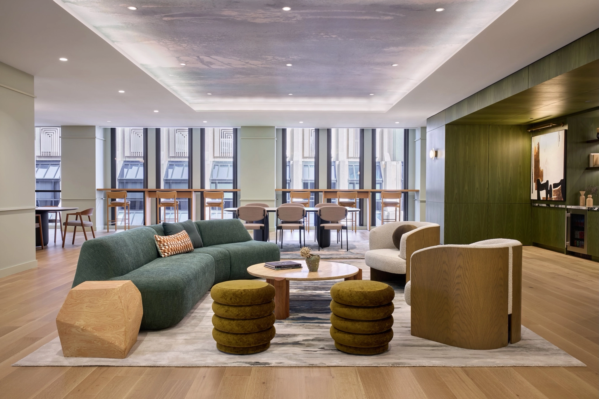 A modern lounge in San Francisco, featuring a workspace vibe with people seated on green sofas and chairs. The room boasts a large window wall and wooden floor. A sign reads "The Cove," complemented by coffee tables and decorative plants—perfect for casual meetings or relaxation.