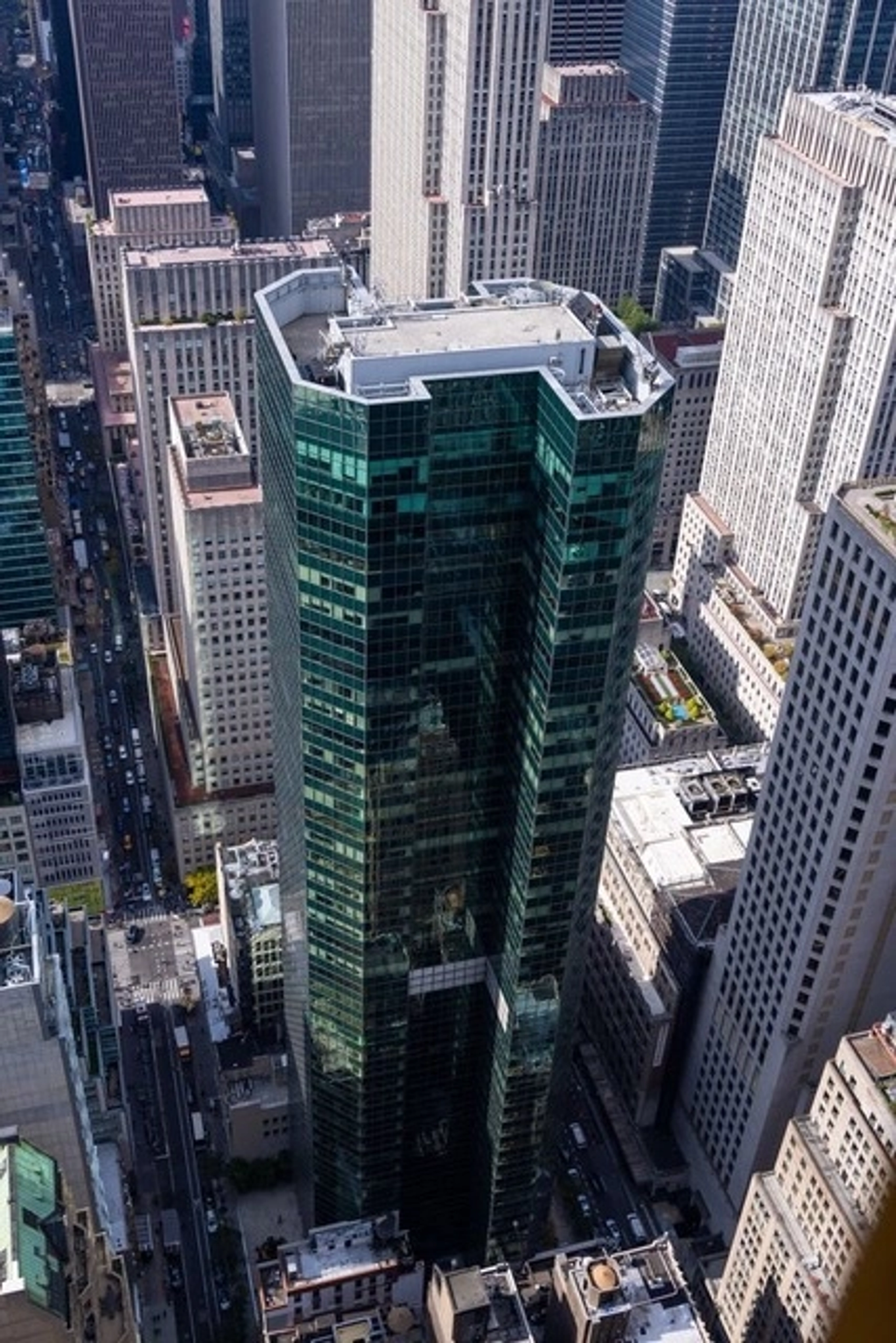 A modern office building in New York with glass windows, metal columns, and benches in a paved outdoor workspace shaded by trees.
