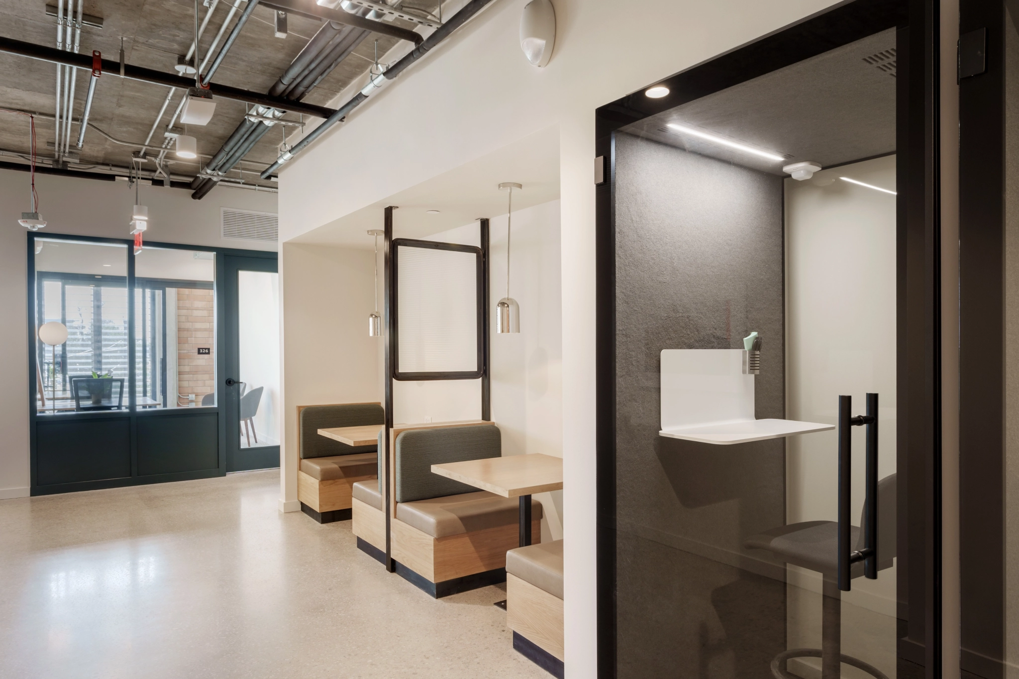 Modern coworking office in Austin featuring an enclosed phone booth and two seating booths. Each booth is equipped with wooden benches and a table, all adorned in elegant gray and white decor, complemented by pendant lighting.