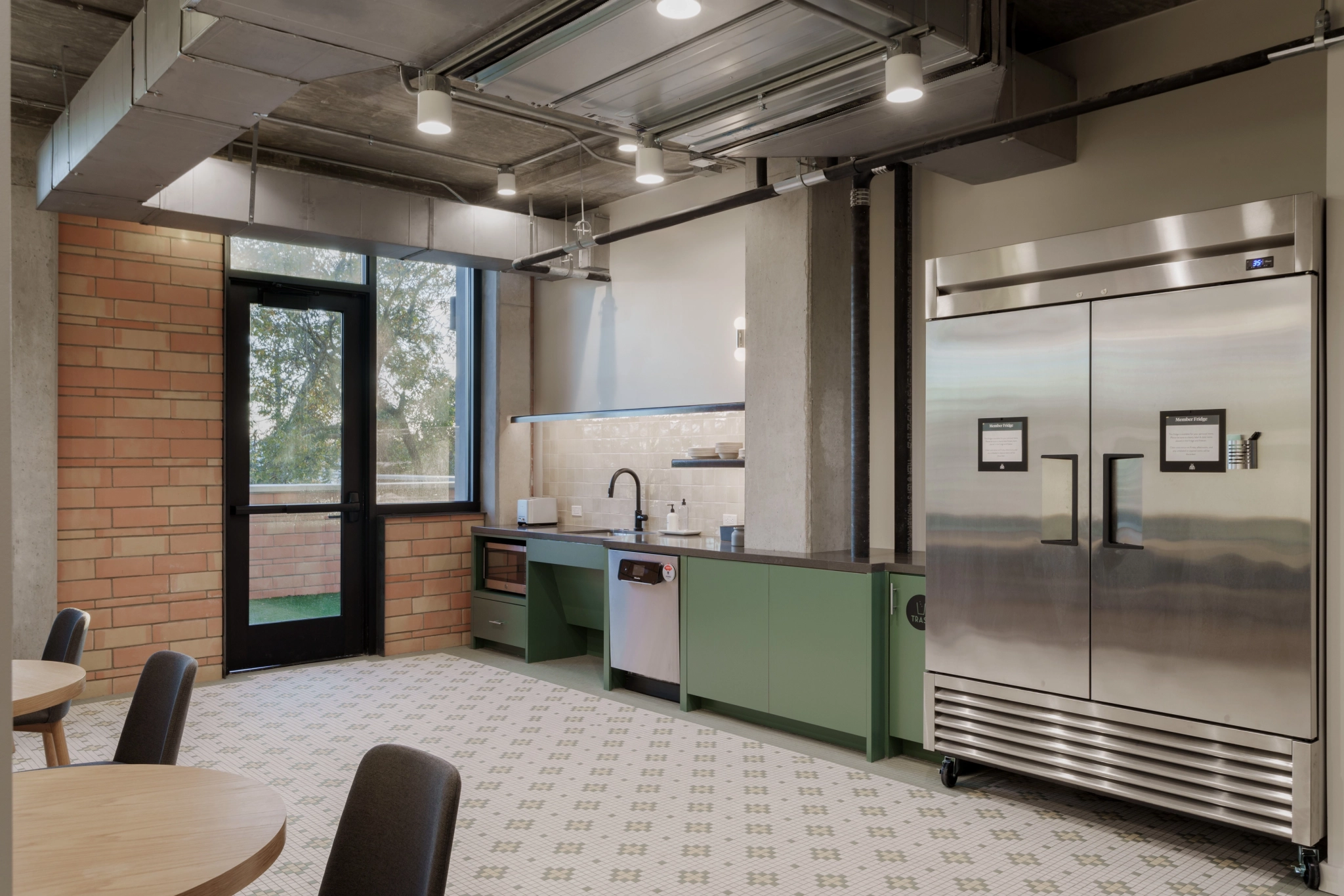 Modern kitchen with green cabinets, stainless steel appliances, and a patterned tile floor. This stylish workspace includes a fridge, dishwasher, sink, microwave, and a brick wall with window—perfect for inspiring culinary creativity.