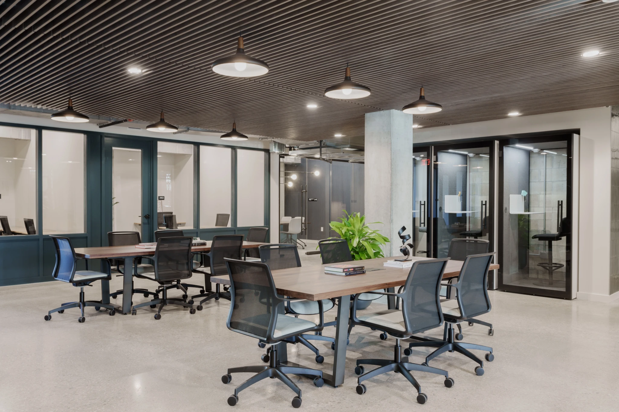 Modern Austin workspace featuring open workstations with black chairs, wood tables and lush plants. Glass-walled meeting rooms face a backdrop of dark wood ceilings adorned with round lights.