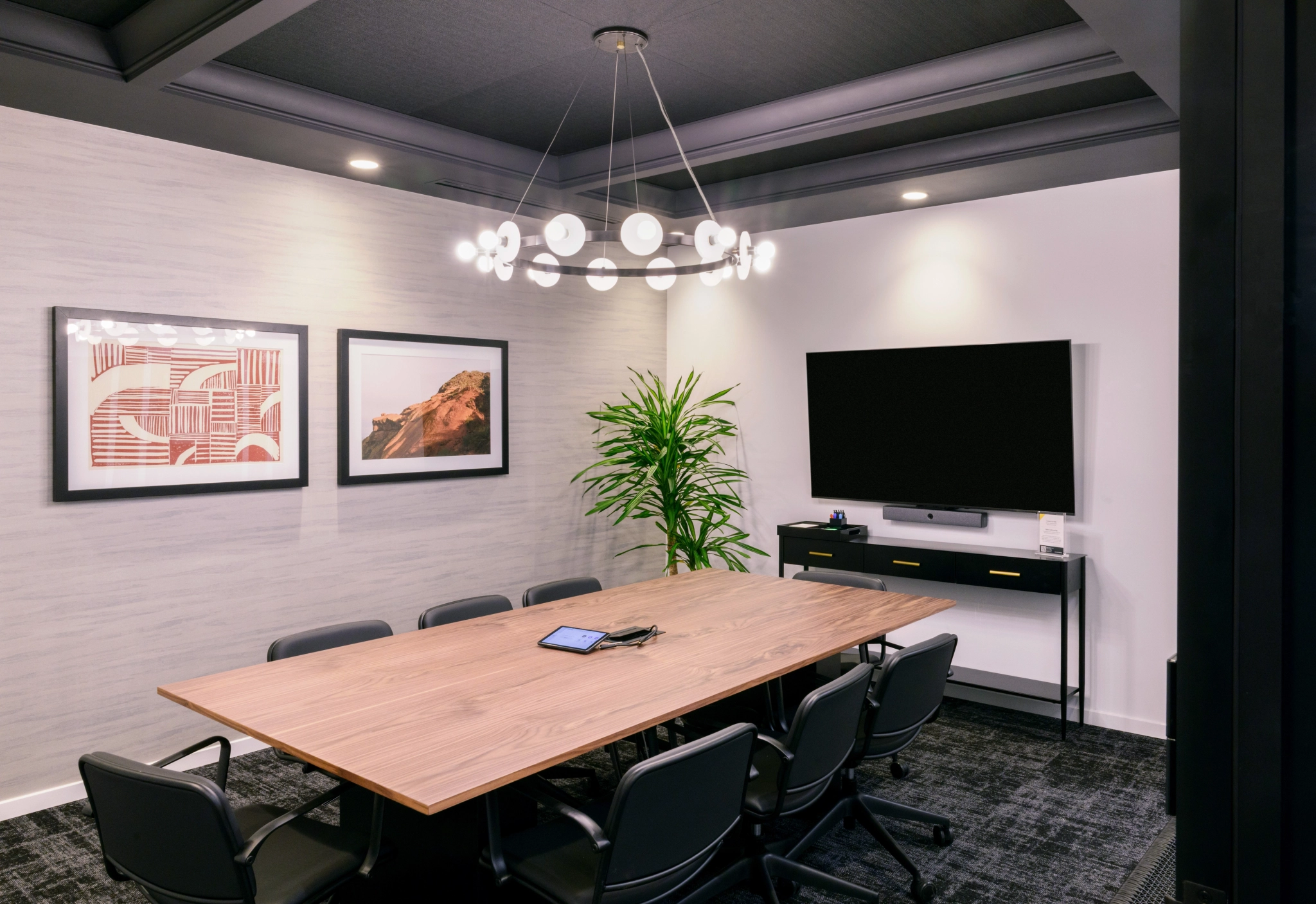 Une salle de conférence moderne de Phoenix avec une table en bois, huit chaises, des œuvres d'art murales, une grande télévision, une plante et un lustre contemporain - parfait pour votre prochaine réunion dans un espace de travail.