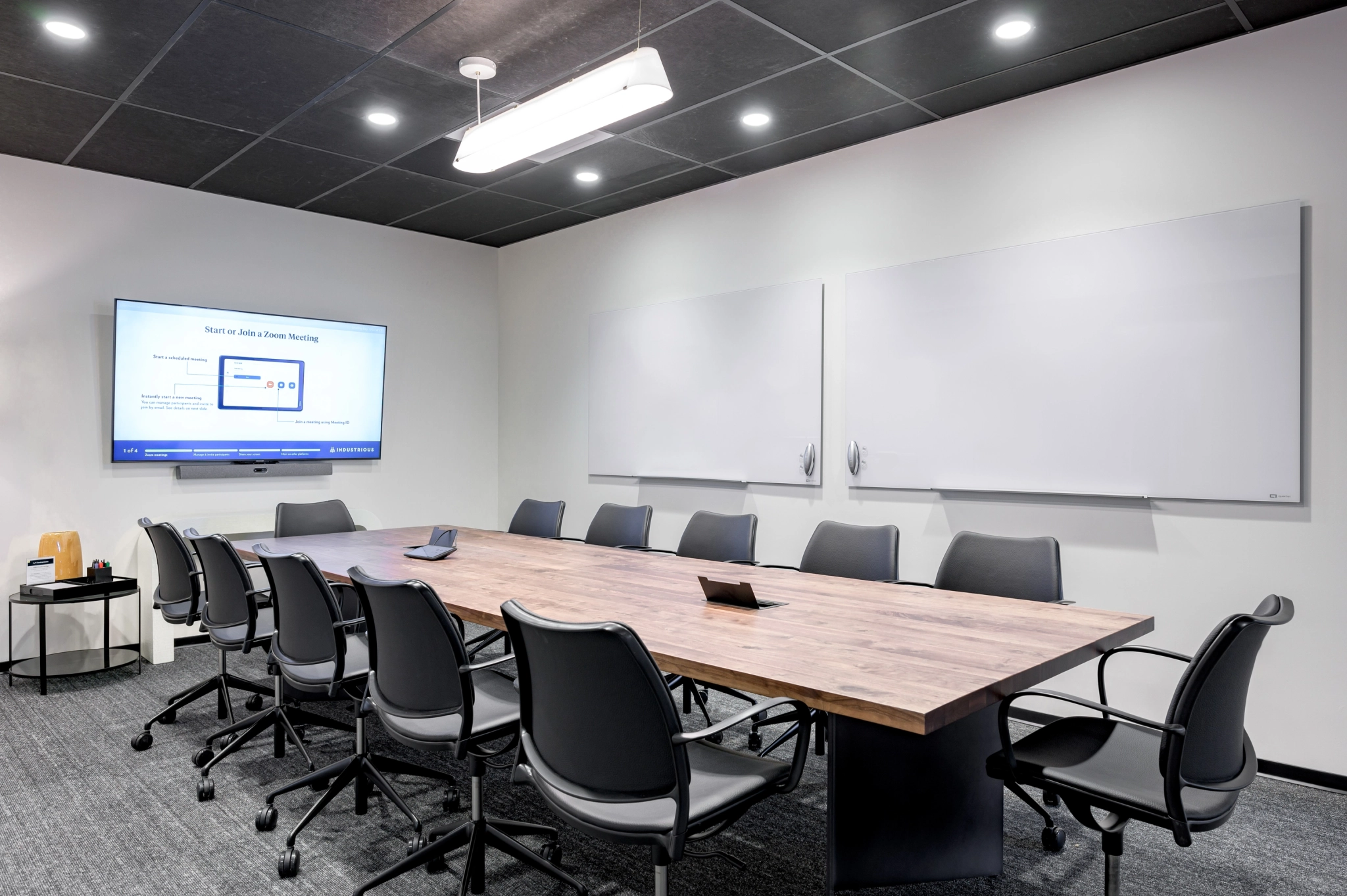 Een moderne vergaderruimte in Austin met een lange houten tafel, zwarte stoelen, een gemonteerd scherm met een presentatie en twee grote whiteboards aan de muur - perfect voor elk kantoorgesprek of brainstormsessie.