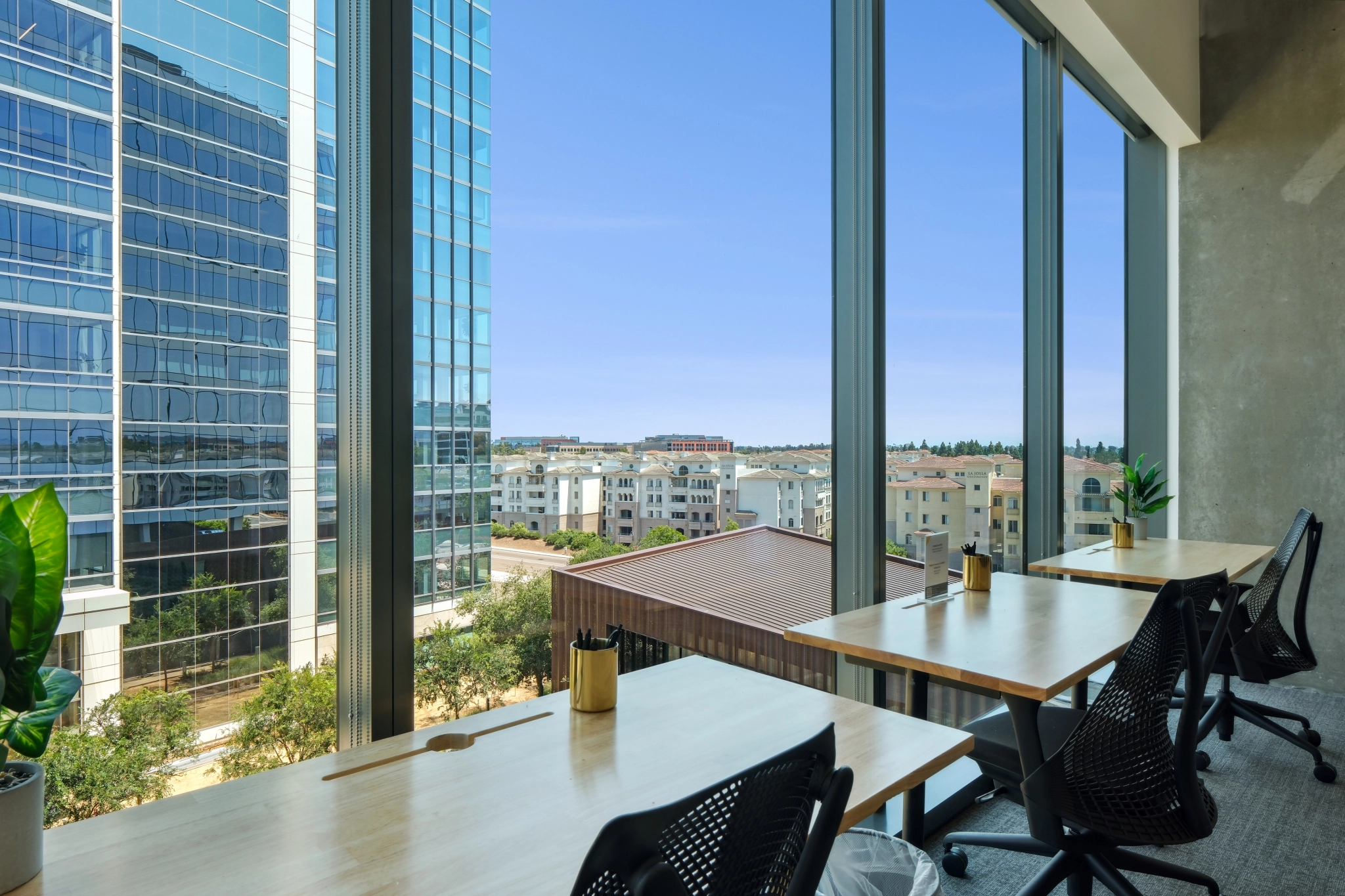 Modern office space in San Diego with large windows, black chairs, and desks overlooking city buildings and a clear blue sky—perfect for a productive workspace or meeting room.