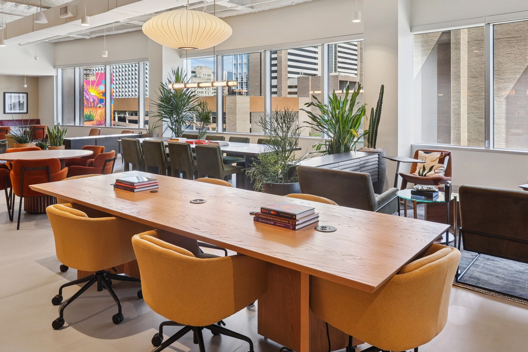 Modern Phoenix office space featuring a large wooden table, vibrant orange swivel chairs, lush indoor plants, and stunning cityscape views through expansive windows—an inspiring workspace for any team.