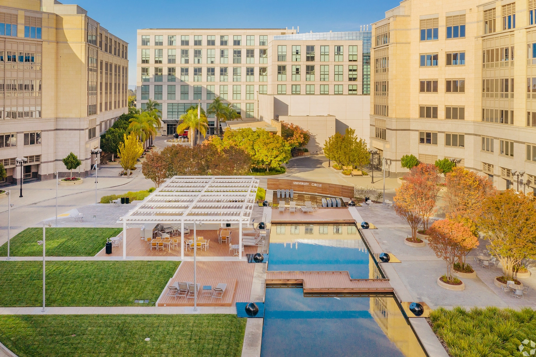 Courtyard with a wooden deck, seating area, small pond, green lawn, and autumn trees, nestled amidst modern office buildings in Palo Alto. A perfect spot for coworking or an informal meeting room atmosphere.