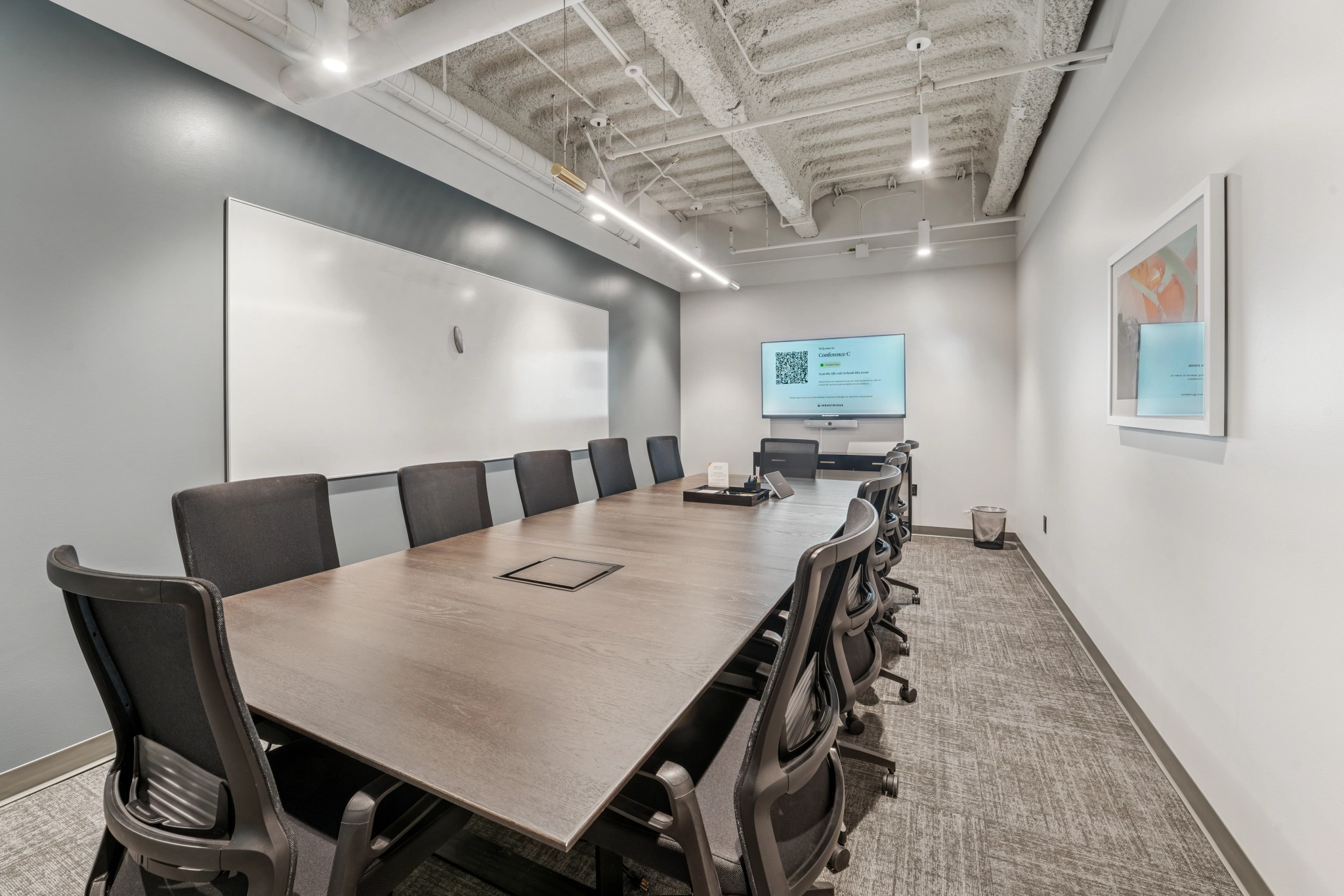 A modern office conference room with a long table, ten chairs, a whiteboard, a wall-mounted screen displaying a presentation, and minimal decor—ideal for meetings in any collaborative workspace.
