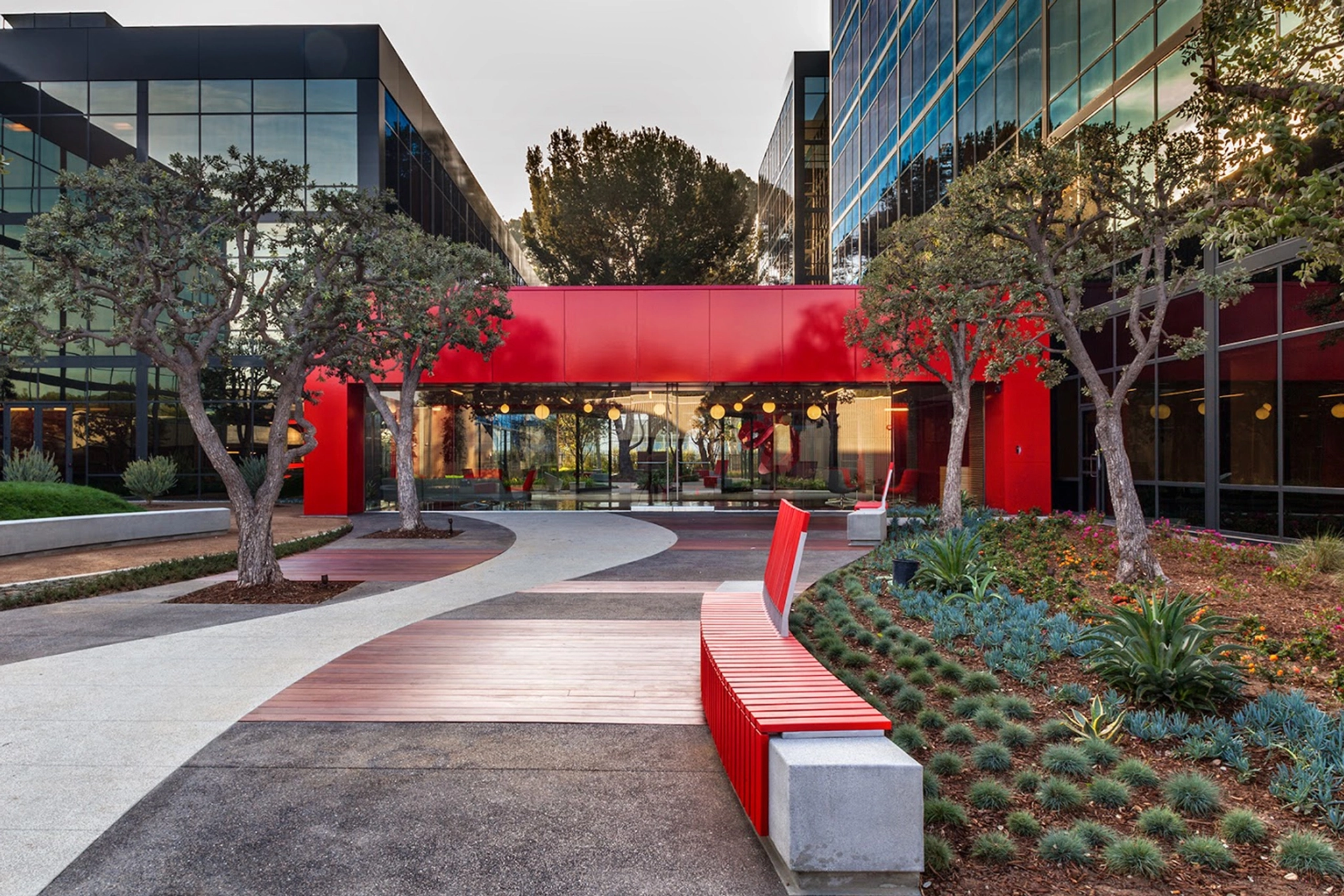 Modernes Bürogebäude in El Segundo mit reflektierendem Glas, rotem Eingang, angelegten Gärten und geschwungenen Gehwegen. Der Raum ist ideal für Coworking und umfasst Bäume und Bänke entlang der Auffahrt.
