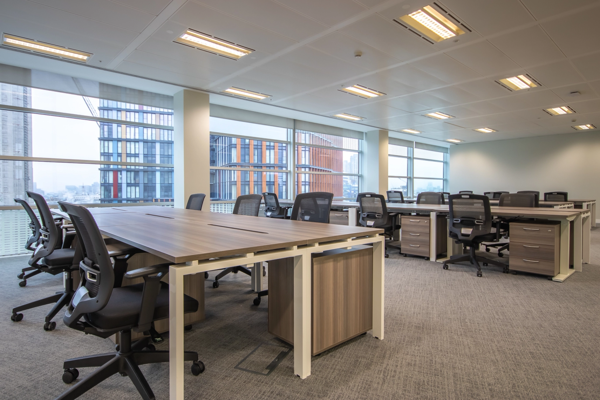 A modern coworking space featuring large windows, multiple desks, and ergonomic chairs in an open layout.