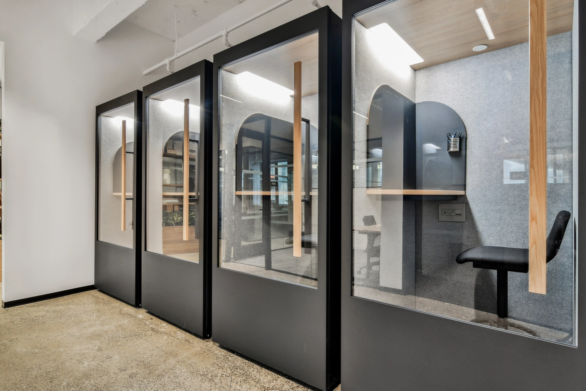 Dans un espace de travail moderne de type "coworking", des bureaux et des chaises en verre sont disposés en rangée le long d'un couloir.