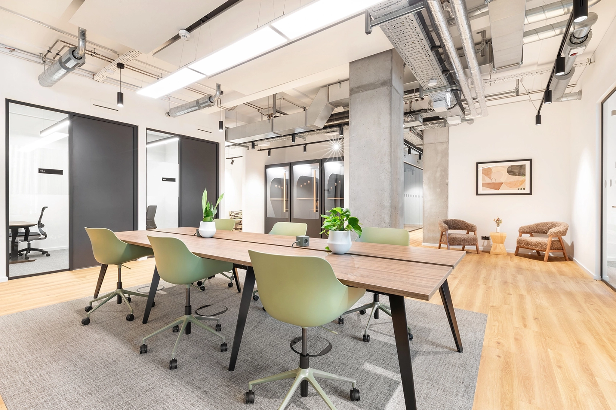A modern Berlin office meeting room with a long wooden table, green chairs, potted plants, and glass-walled offices in the background.