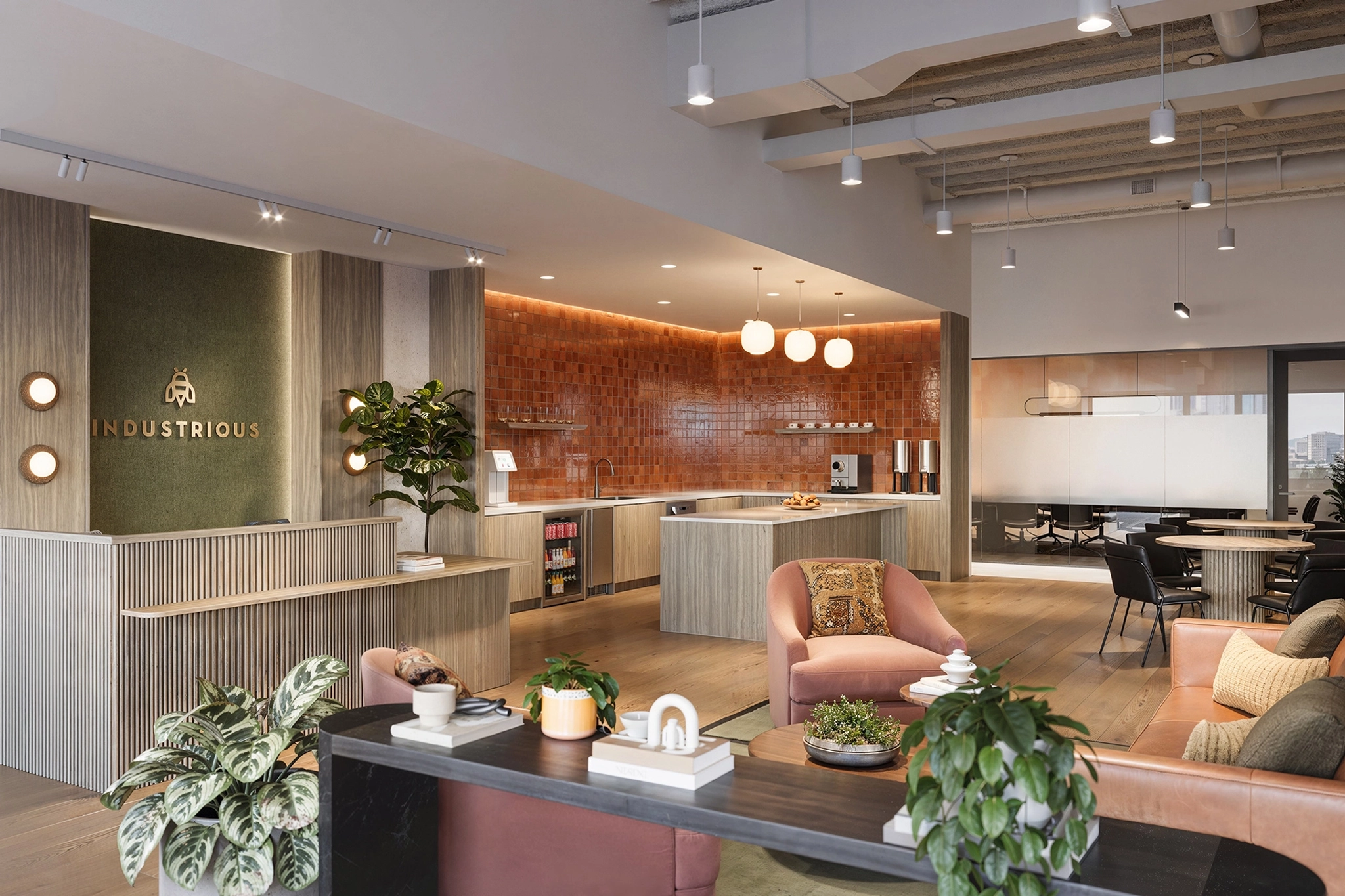 Modern coworking space in Burbank featuring lounge seating, plants, a coffee bar, and a meeting room in the background under warm lighting.