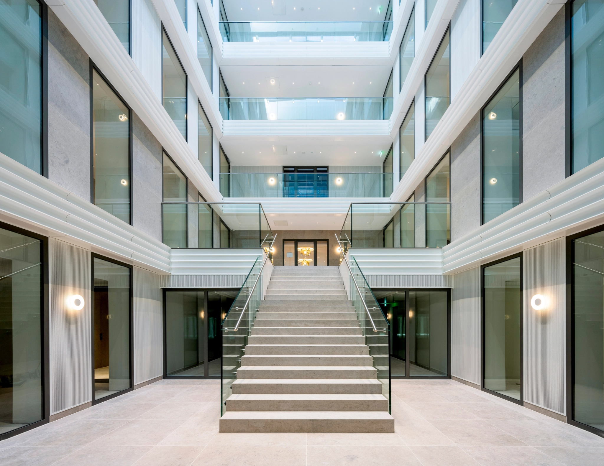 Modern indoor atrium in an Amsterdam office featuring a wide central staircase, glass railings, multiple floors with balconies, and minimalist workspace design elements.