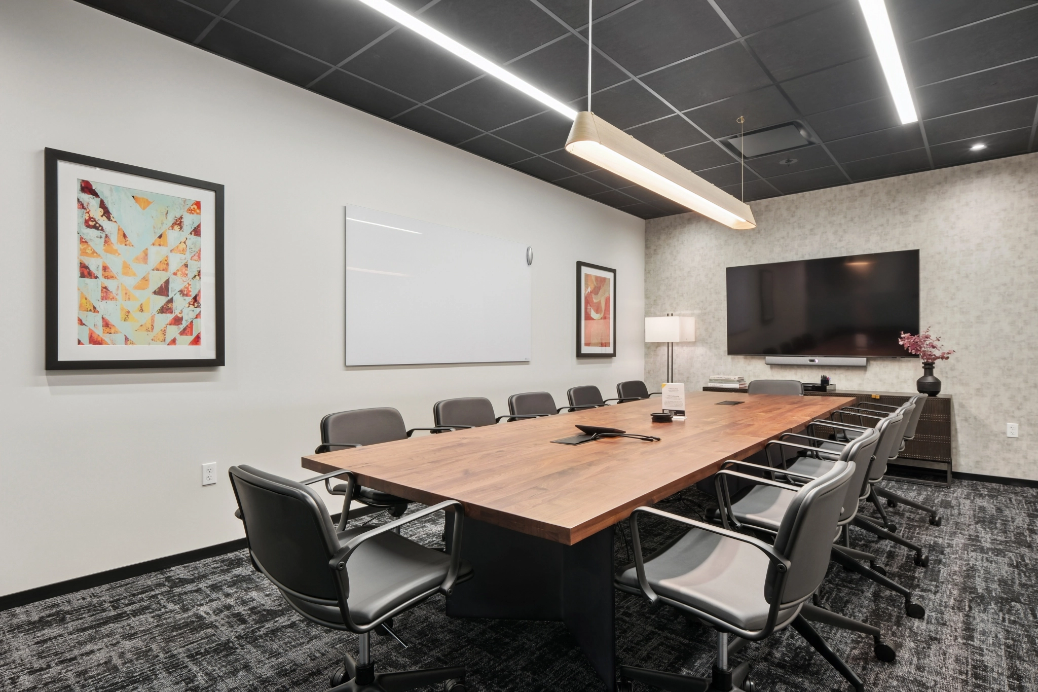 Modernes Besprechungszimmer in New York mit einem langen Holztisch, zehn Stühlen, einem großen Wandbildschirm, einem Whiteboard, einer Lampe und gerahmten Kunstwerken - perfekt für jeden professionellen Arbeitsbereich.
