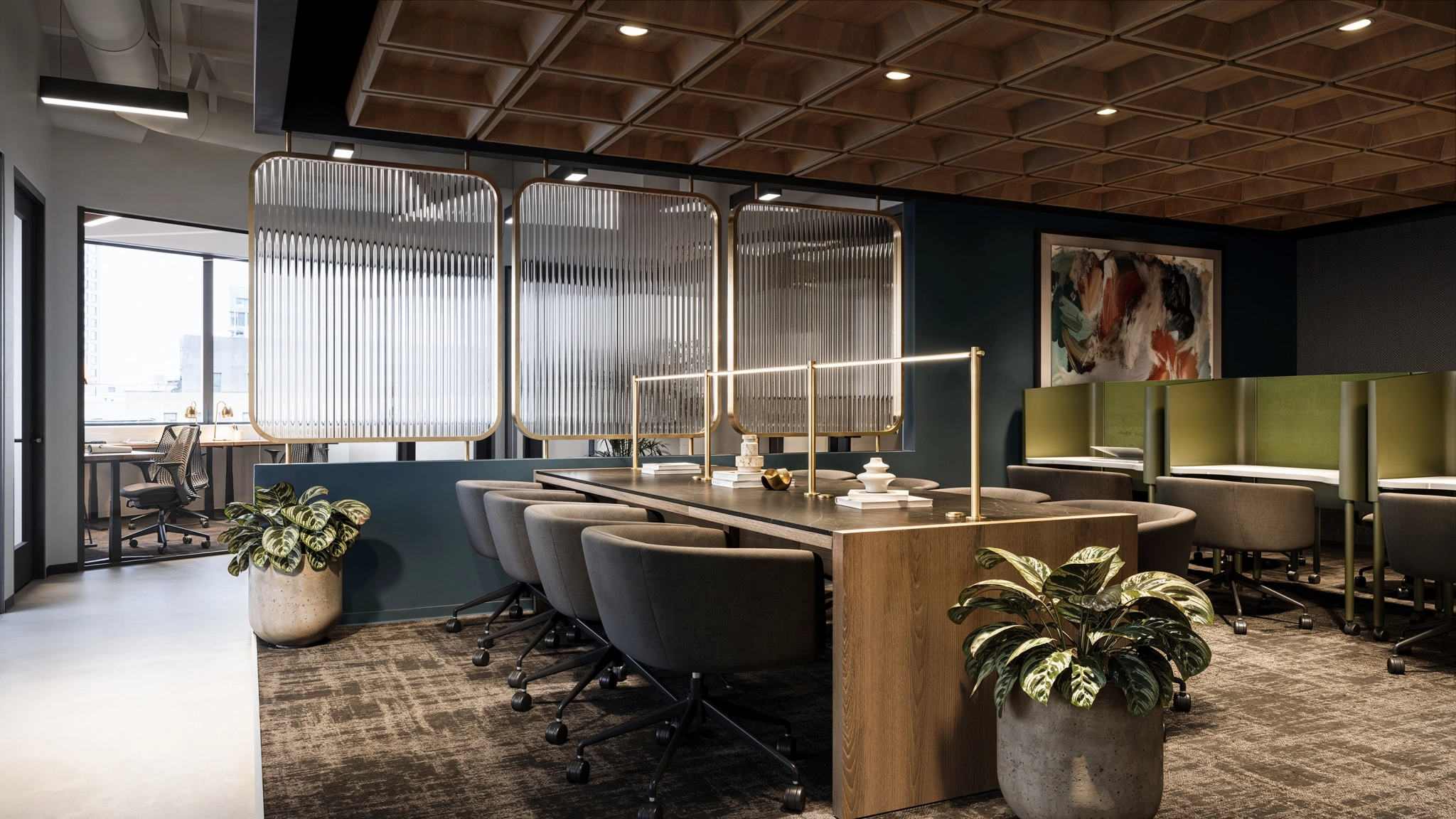 Modern office workspace featuring a long table, gray chairs, green divider cubicles, potted plants, and abstract wall art; natural light streams in from windows on the left.